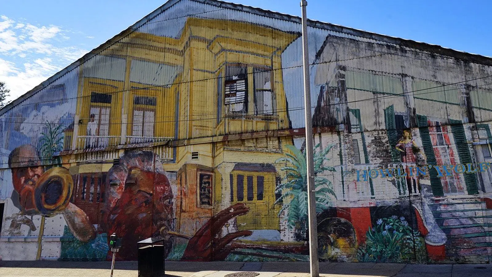 Colorful mural on urban street wall featuring musical instruments, people, and yellow building under clear sky.