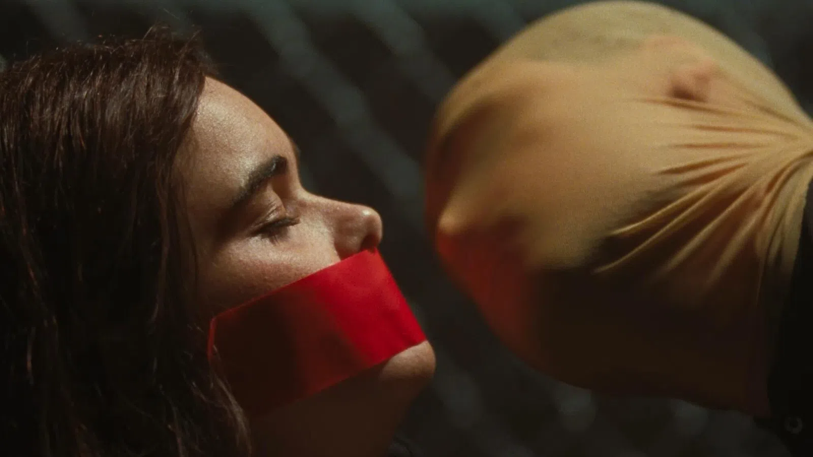 Woman with red tape over her mouth faces a person with a stocking mask over their head in a tense scene.