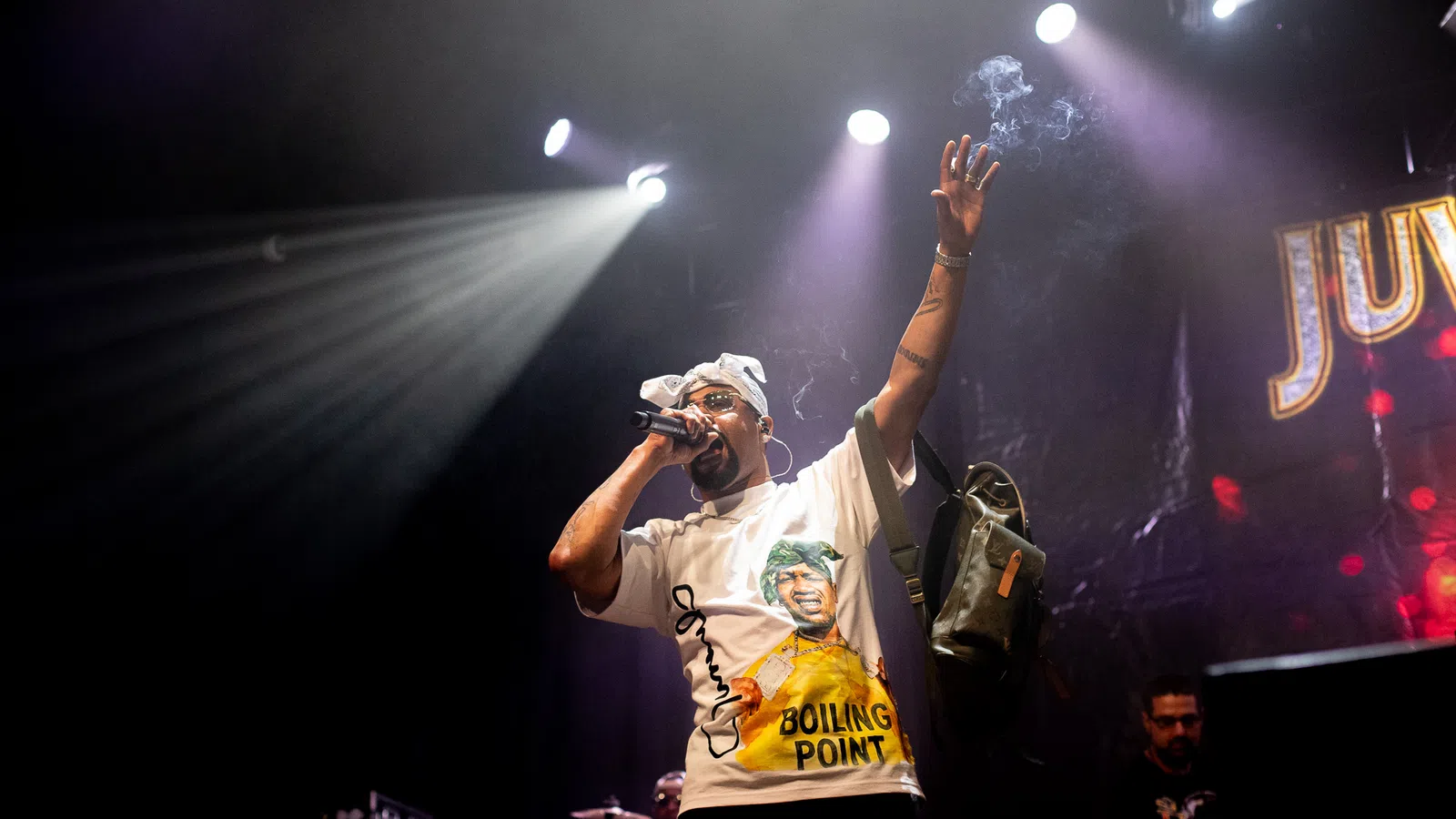 Hip hop artist performing on stage under bright spotlights with microphone and raised arm during concert.