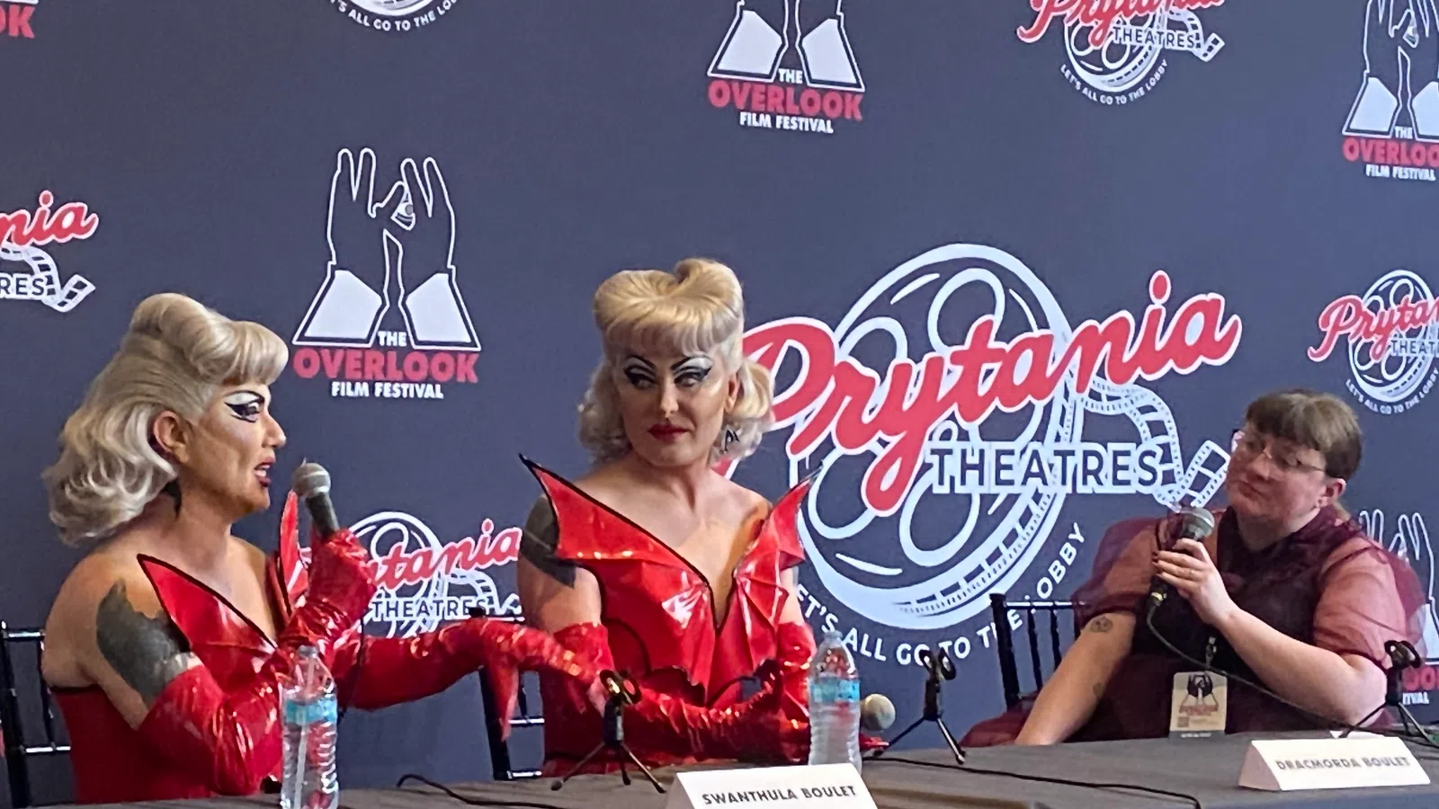 Two performers in red costumes speak at a panel with a moderator at Prytania Theatres for Overlook Film Festival.