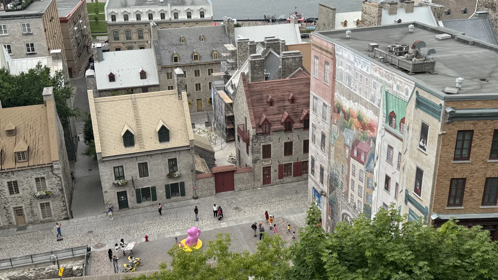 Historic stone buildings and cobblestone streets near waterfront with mural and green trees