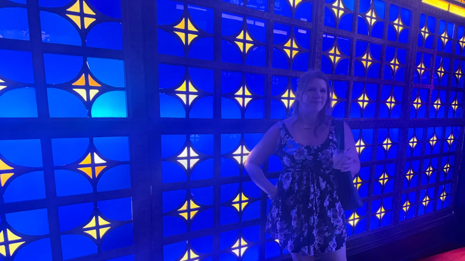 Woman in a floral dress standing in front of a vibrant blue and yellow patterned illuminated wall.