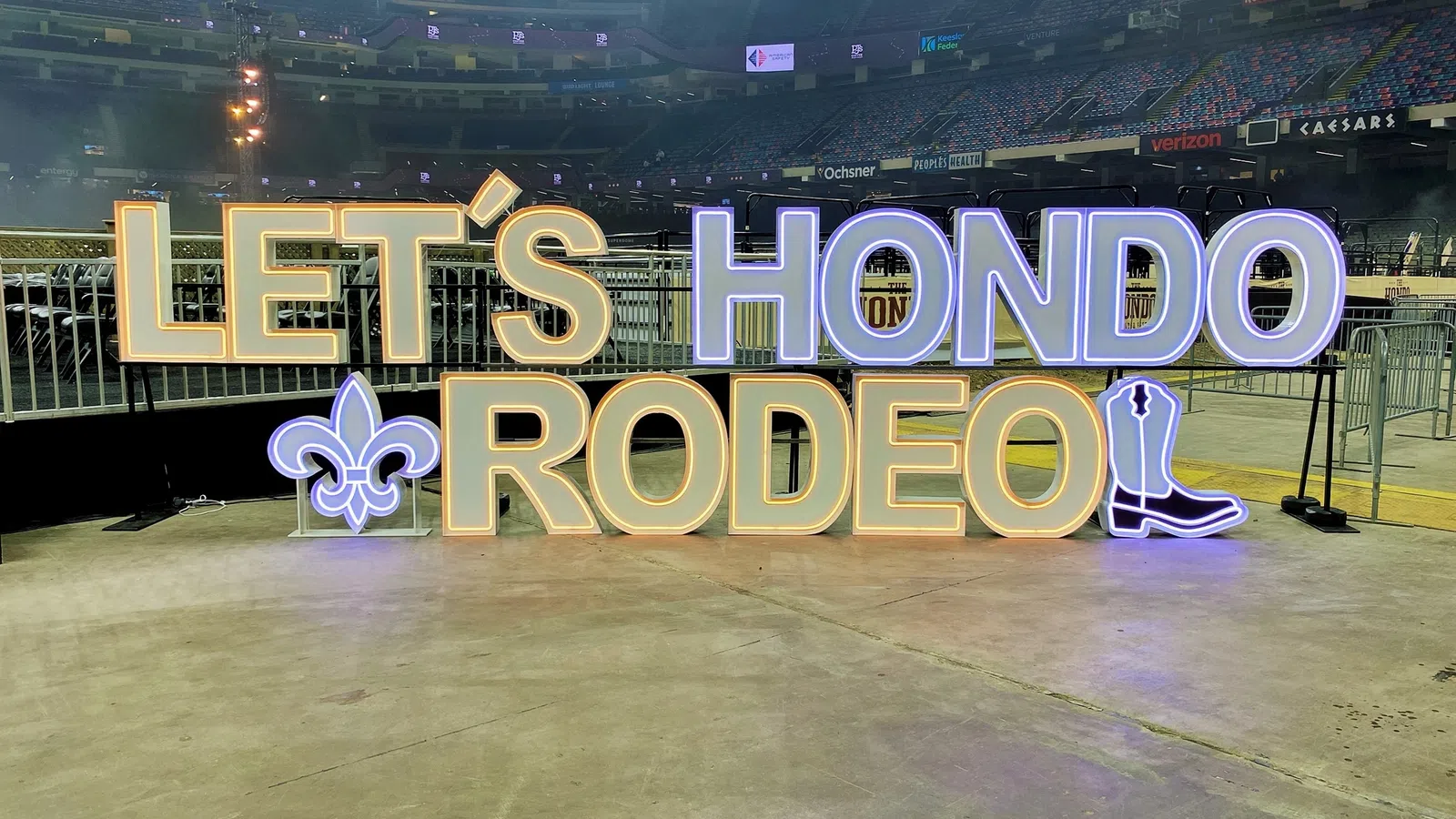 Illuminated sign reading LET'S HONDO RODEO with fleur-de-lis and cowboy boot icons on stadium floor.