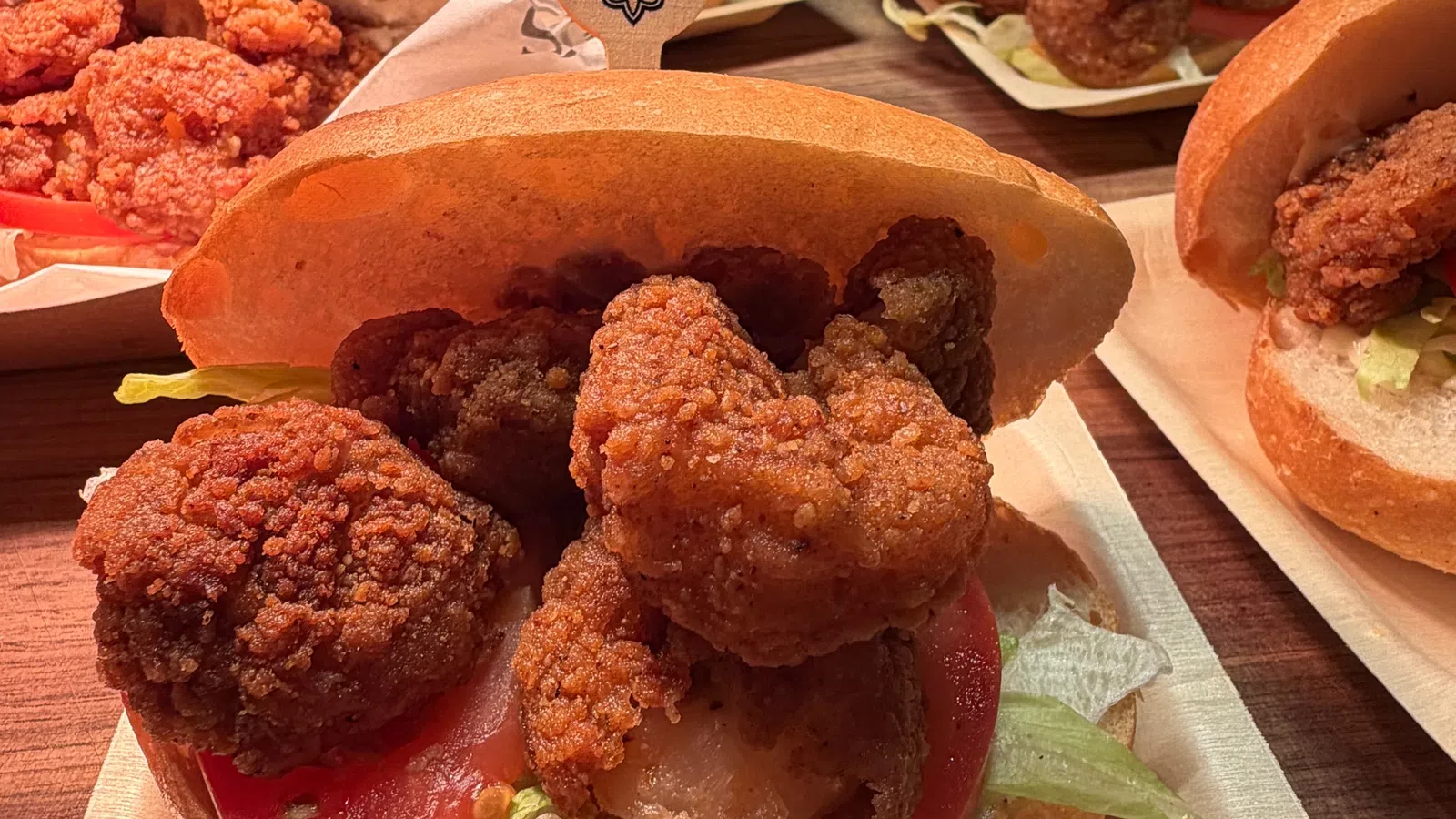 Close-up of fried shrimp po'boy sandwiches with lettuce and tomato on buns on wooden table