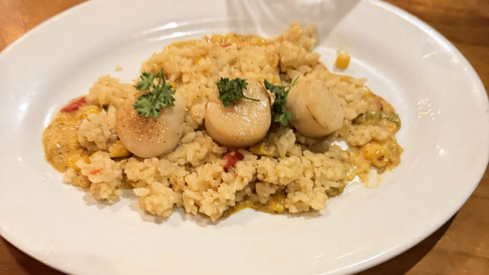 Plate of creamy risotto with three seared scallops and parsley garnish on a rustic wooden table.