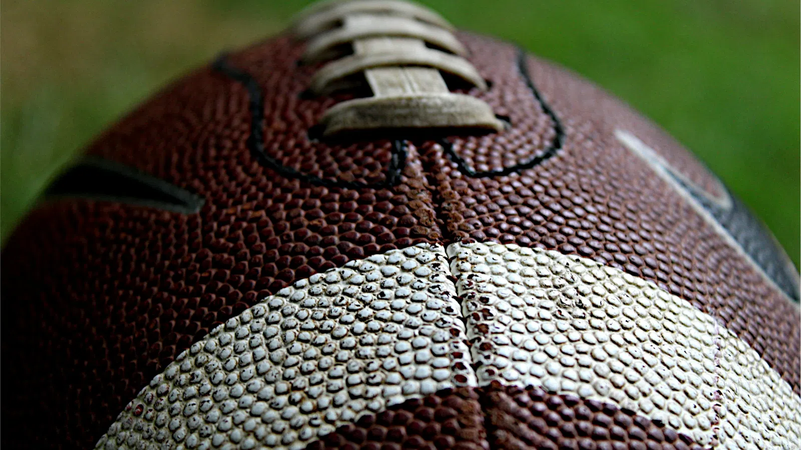 Close-up of a textured brown and white American football showing laces and pebbled surface detail.