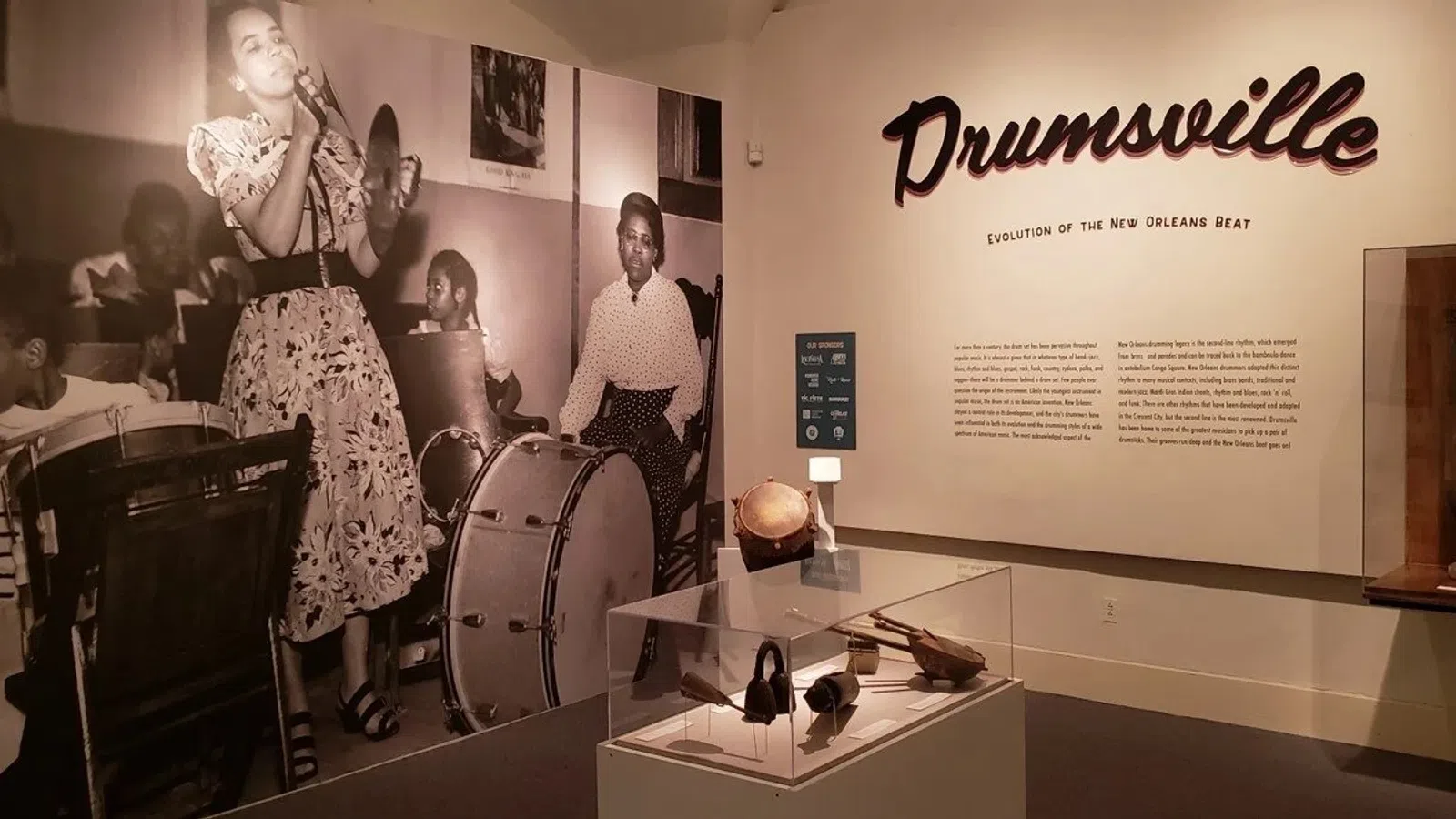 Exhibit showcasing the evolution of New Orleans beat with vintage jazz band photo and percussion instruments.