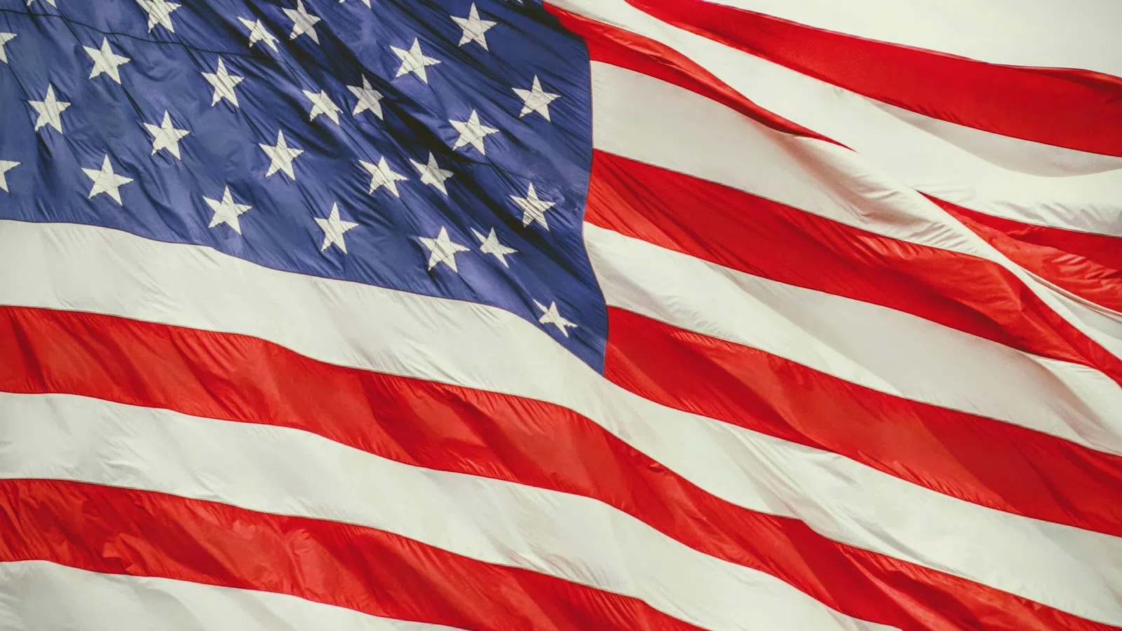 Waving American flag with red and white stripes and white stars on a blue field against sky.