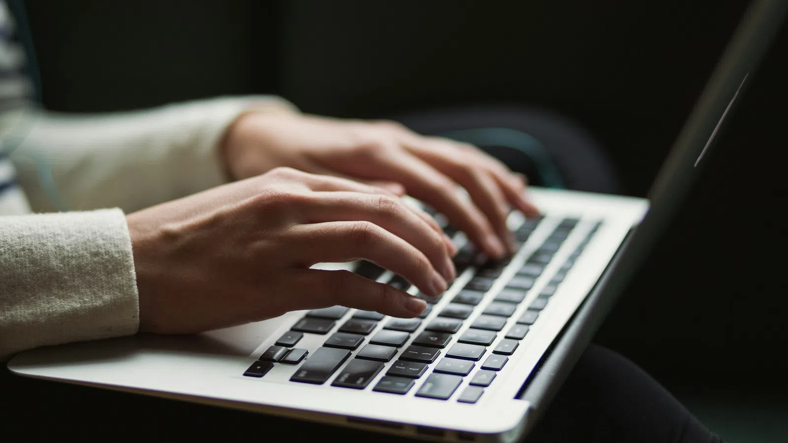 Close-up of hands typing on a laptop keyboard in a dimly lit environment with focused activity.