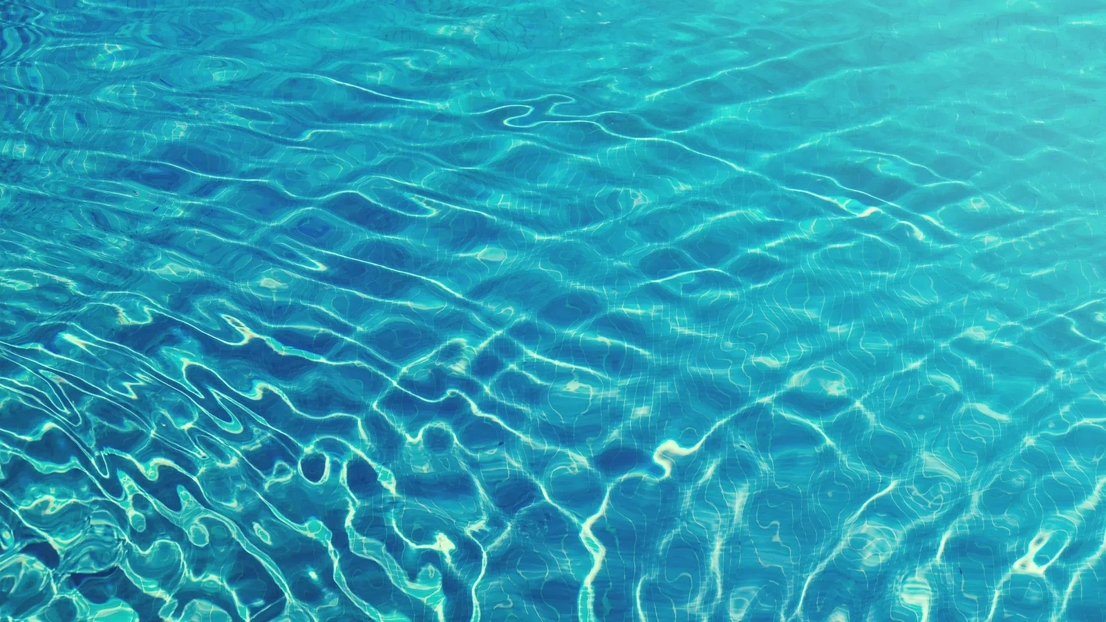 Clear blue water surface with ripples reflecting sunlight creating dynamic patterns