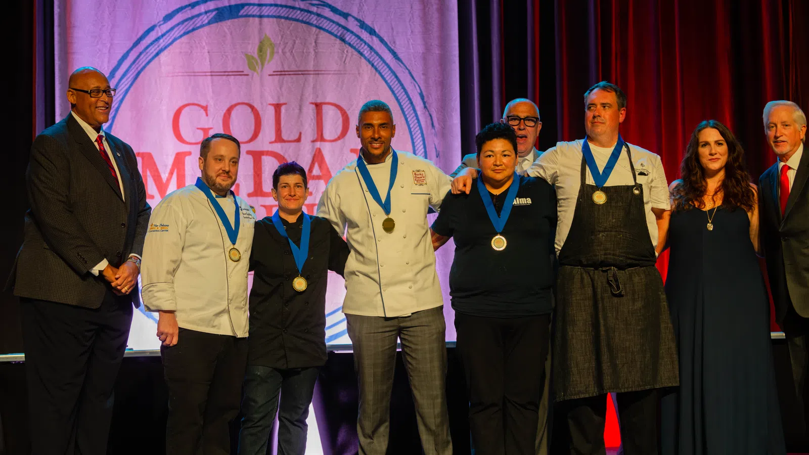 Group of chefs and officials posing with medals on stage at Gold Medal Plate culinary competition event.