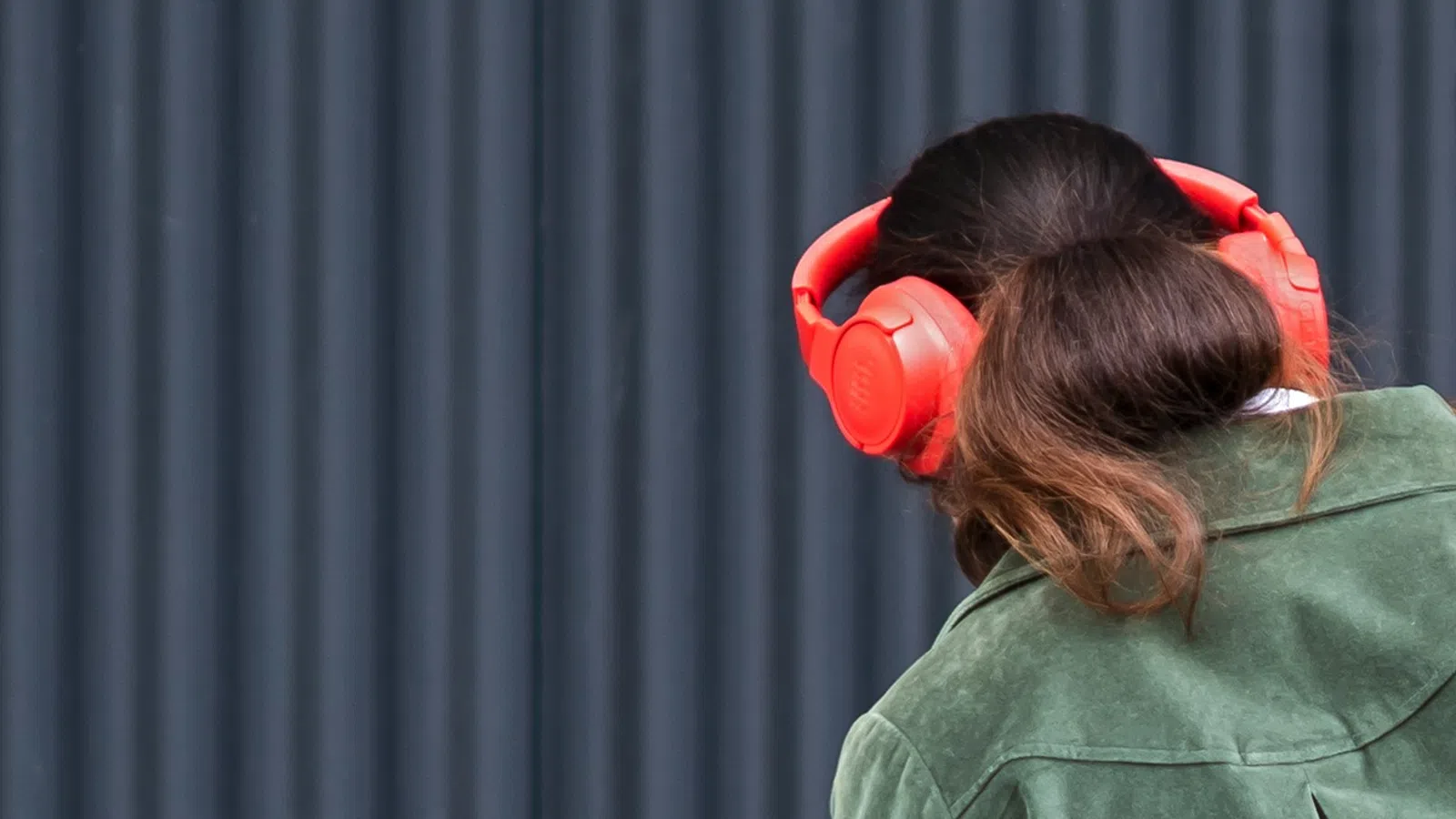 Woman with brown hair wearing a green jacket and bright red over-ear headphones against a dark background