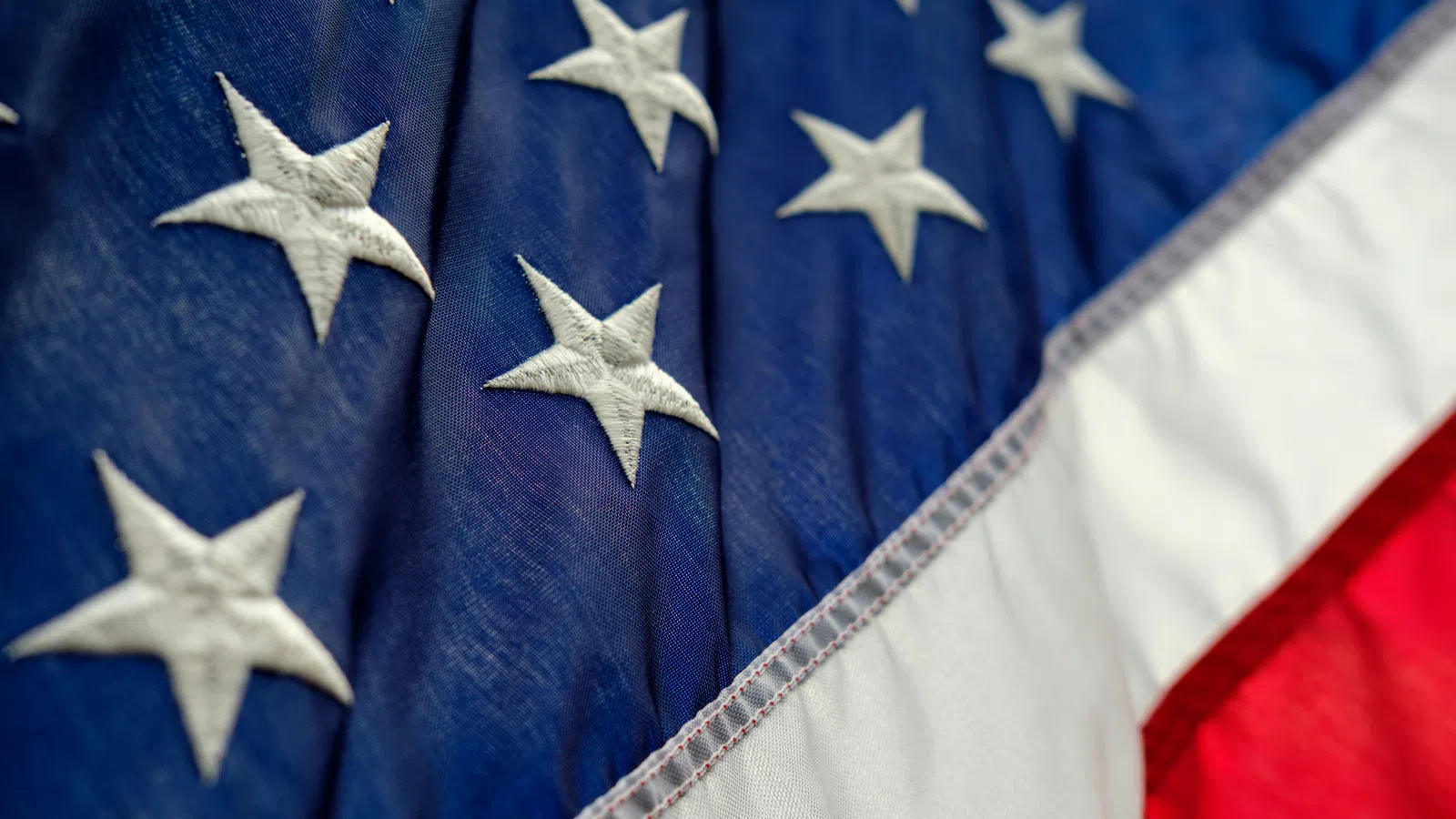 Close-up of the American flag showing embroidered white stars on blue and red and white stripes.