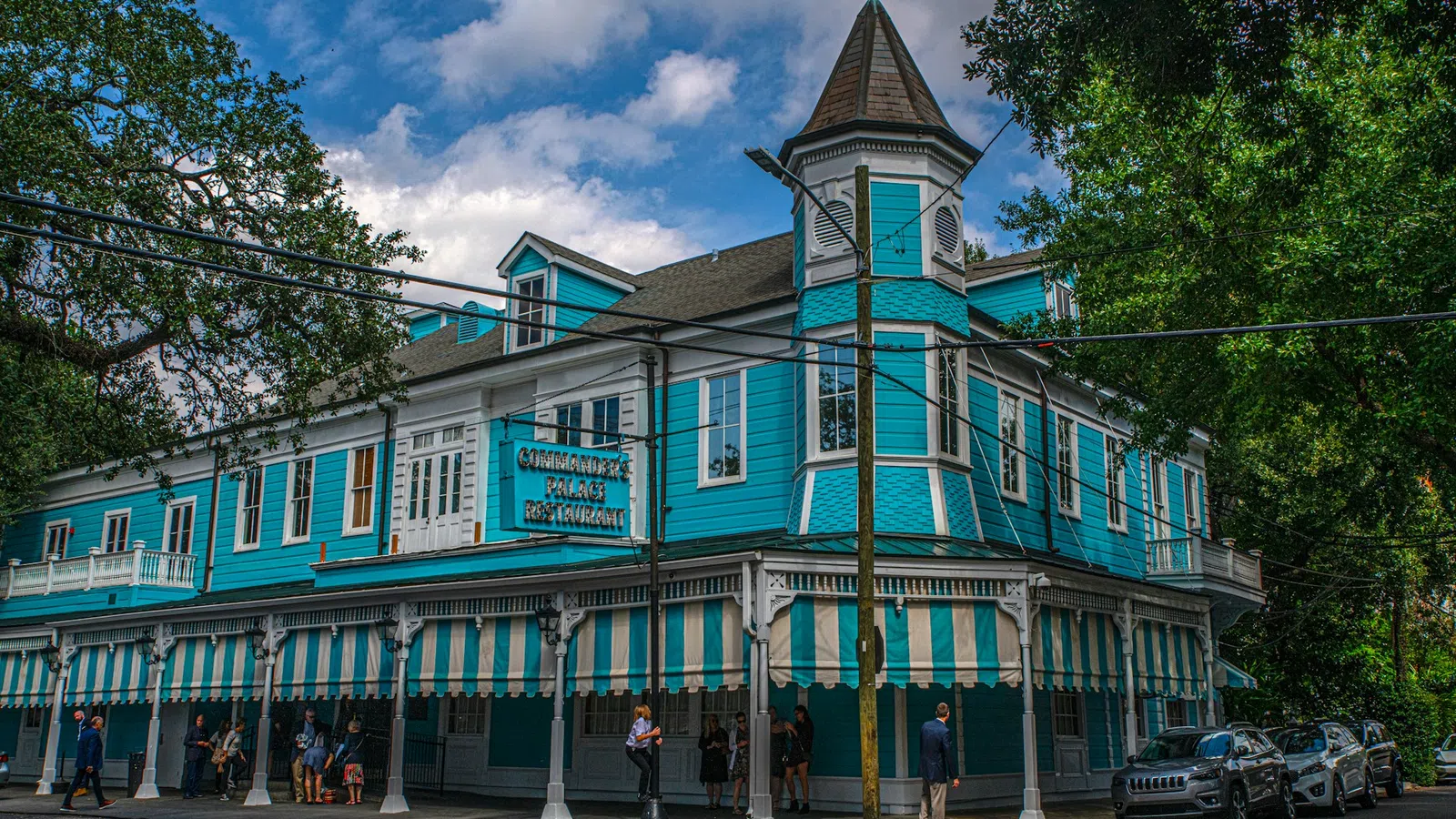 Historic turquoise and white two-story restaurant with striped awnings and pointed turret under a blue sky.