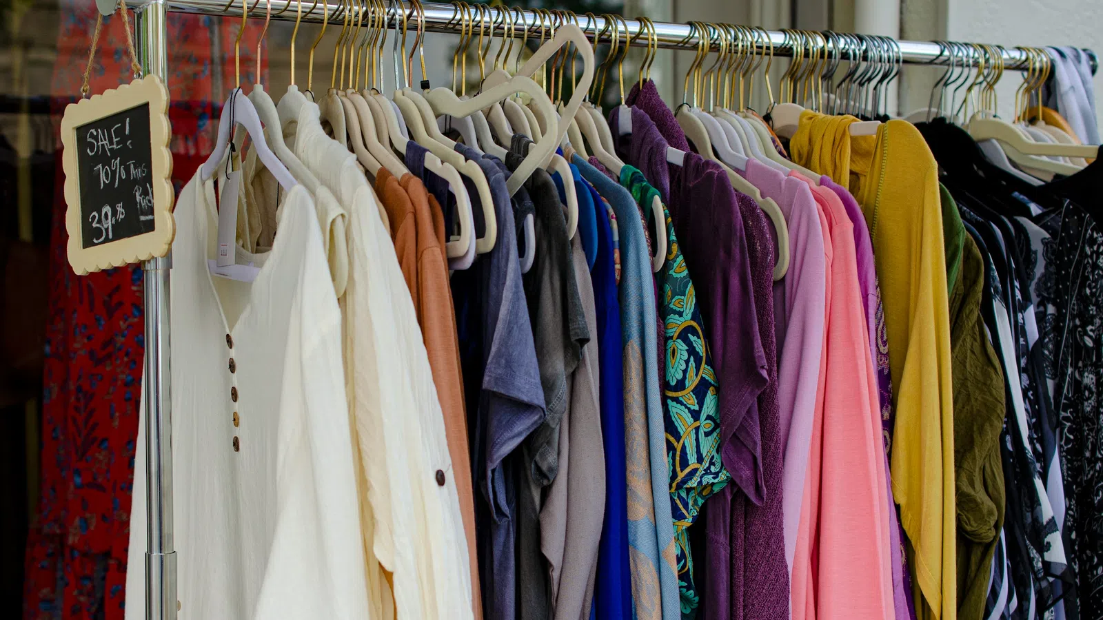Clothing rack with diverse shirts and sweaters in various colors, with overlaid chalkboard sign showing sale details.