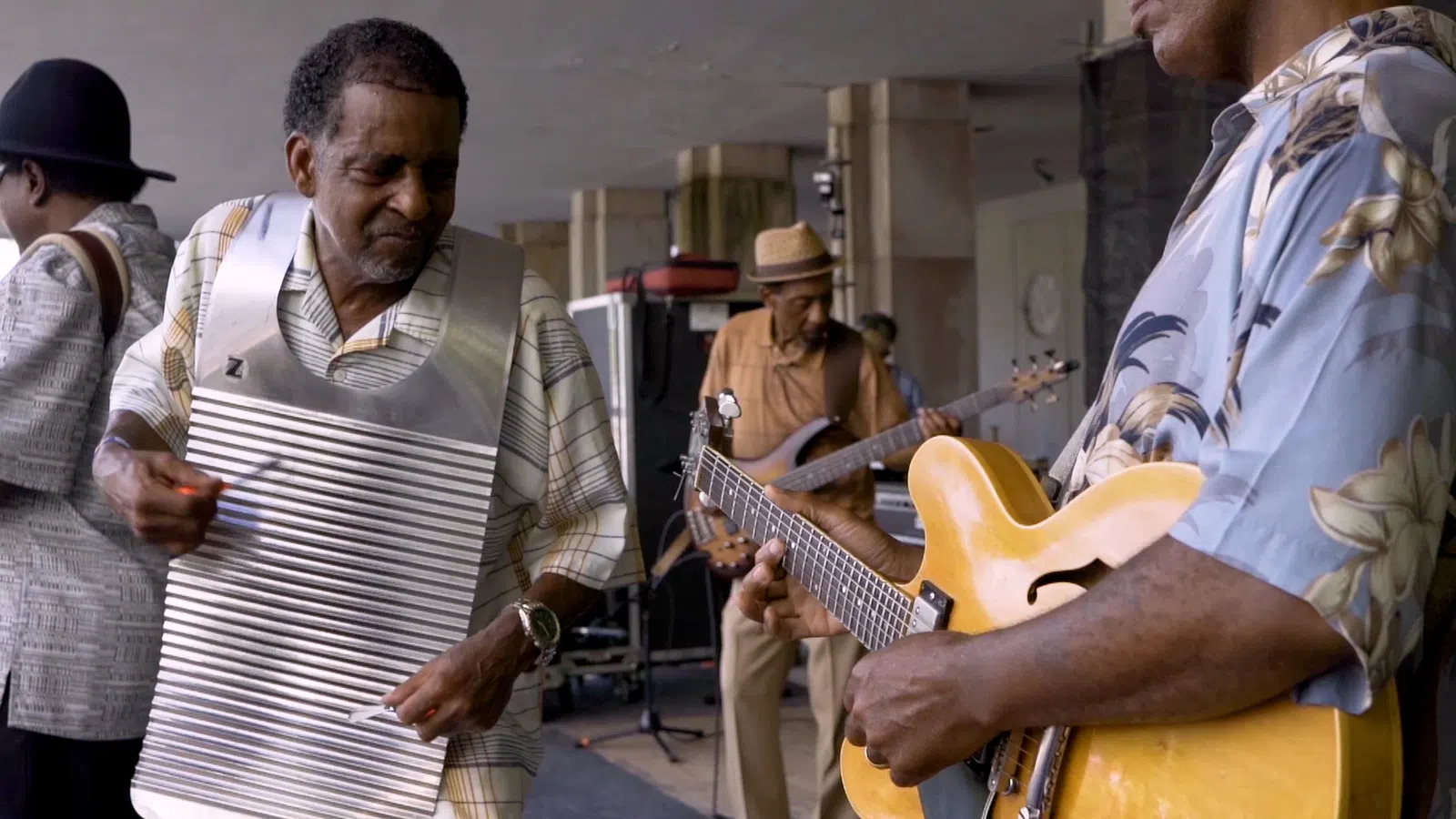 Group of musicians playing guitar, bass, and washboard in a lively outdoor setting.