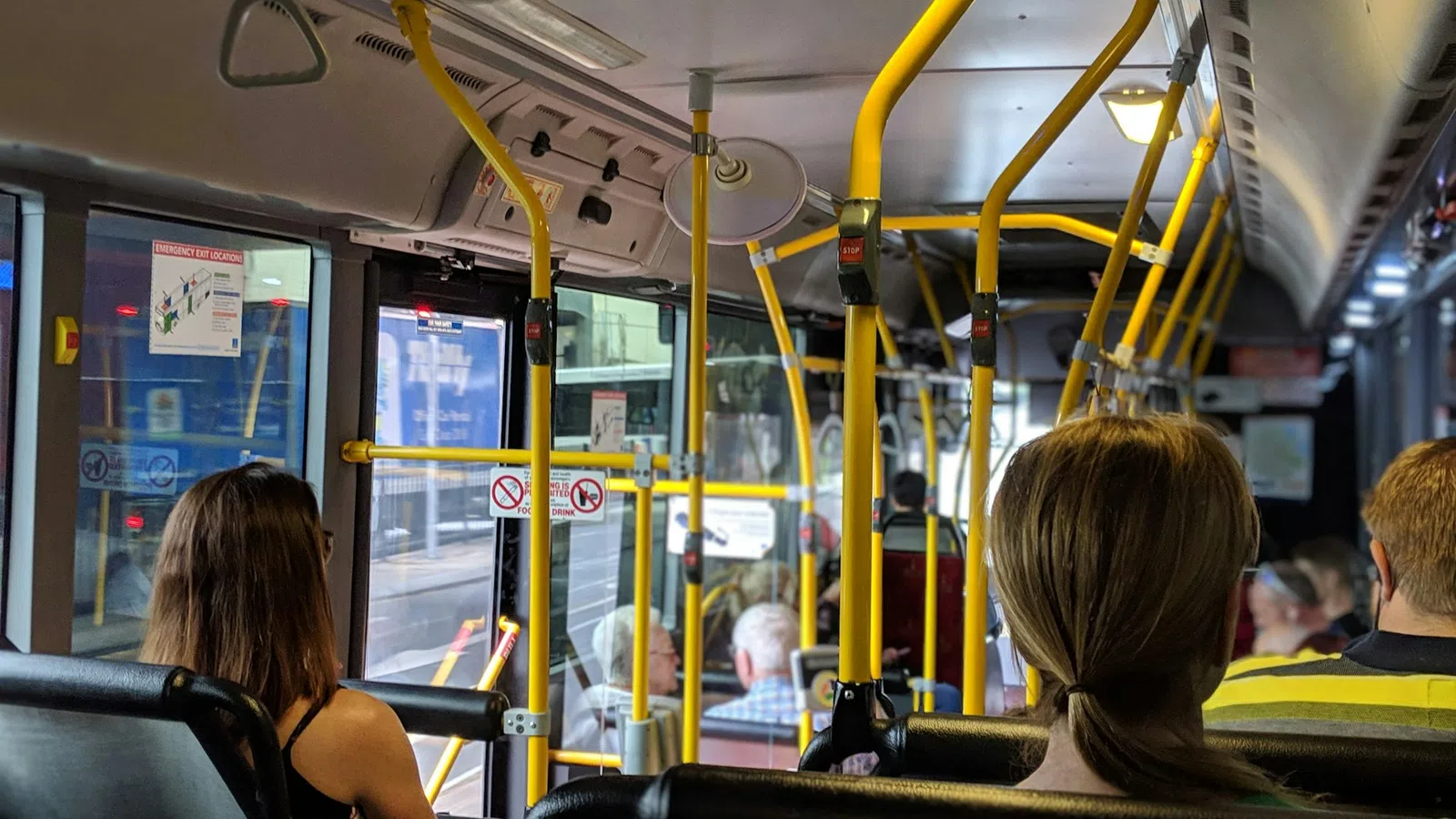 Passengers seated inside a city bus with yellow handrails and windows showing an urban street outside.