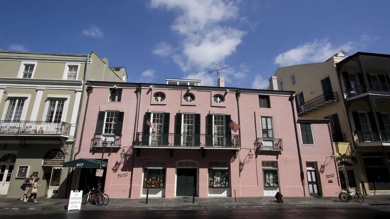 Historic pink building with green shutters and balconies under a blue sky with scattered clouds.