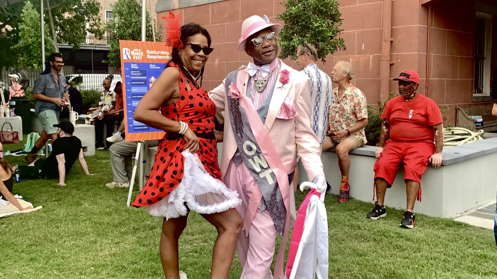 Couple dressed in vibrant retro outfits enjoying an outdoor festival on a sunny day with people relaxing nearby