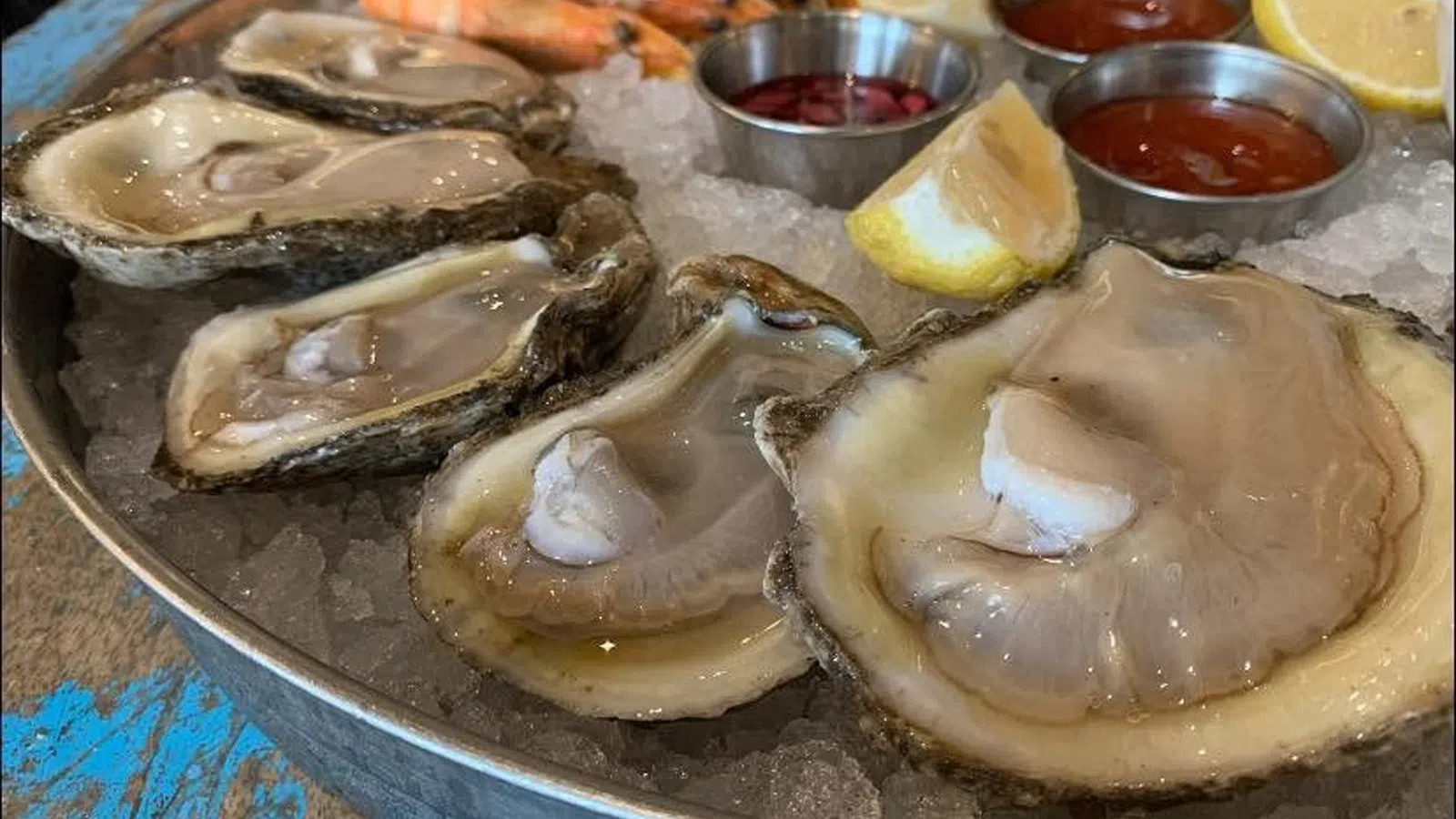 Fresh oysters and shrimp on ice served with lemon wedges and cocktail sauces on a metal platter.