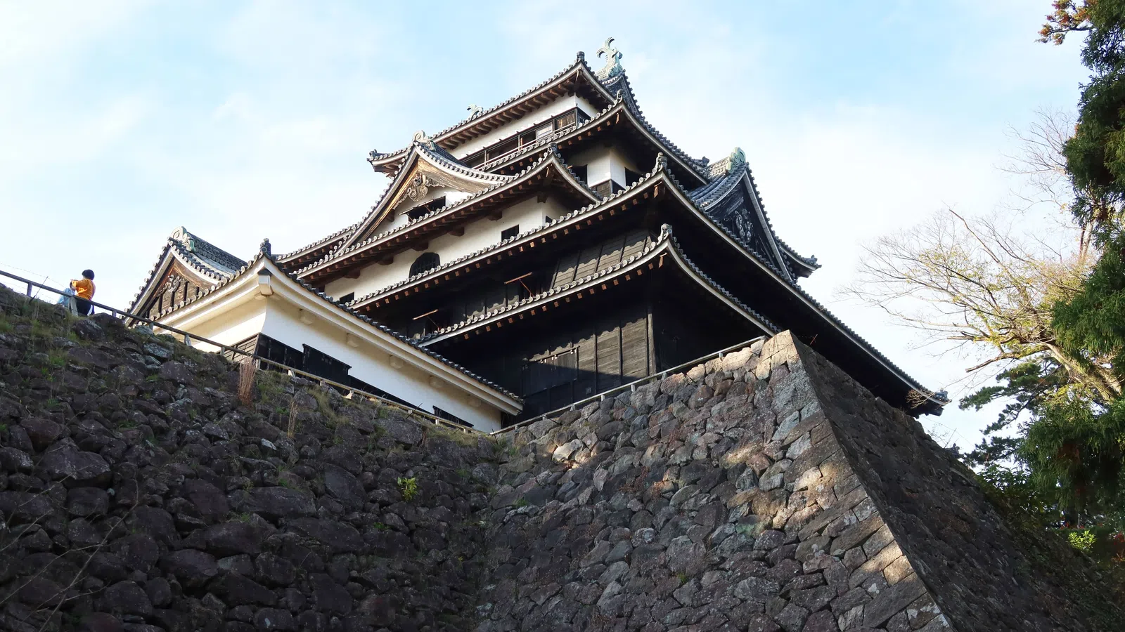 Traditional Japanese castle with multi-tiered roofs atop large stone walls under a clear sky.