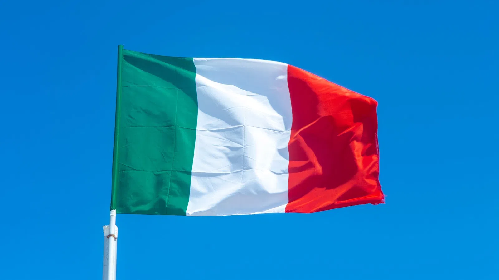 Italy national flag waving against a clear blue sky background outdoors.