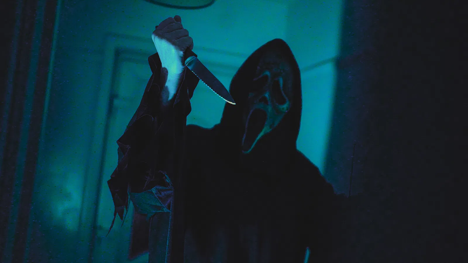 Person wearing a ghost face mask and dark robe holding a raised knife in a dimly lit room.