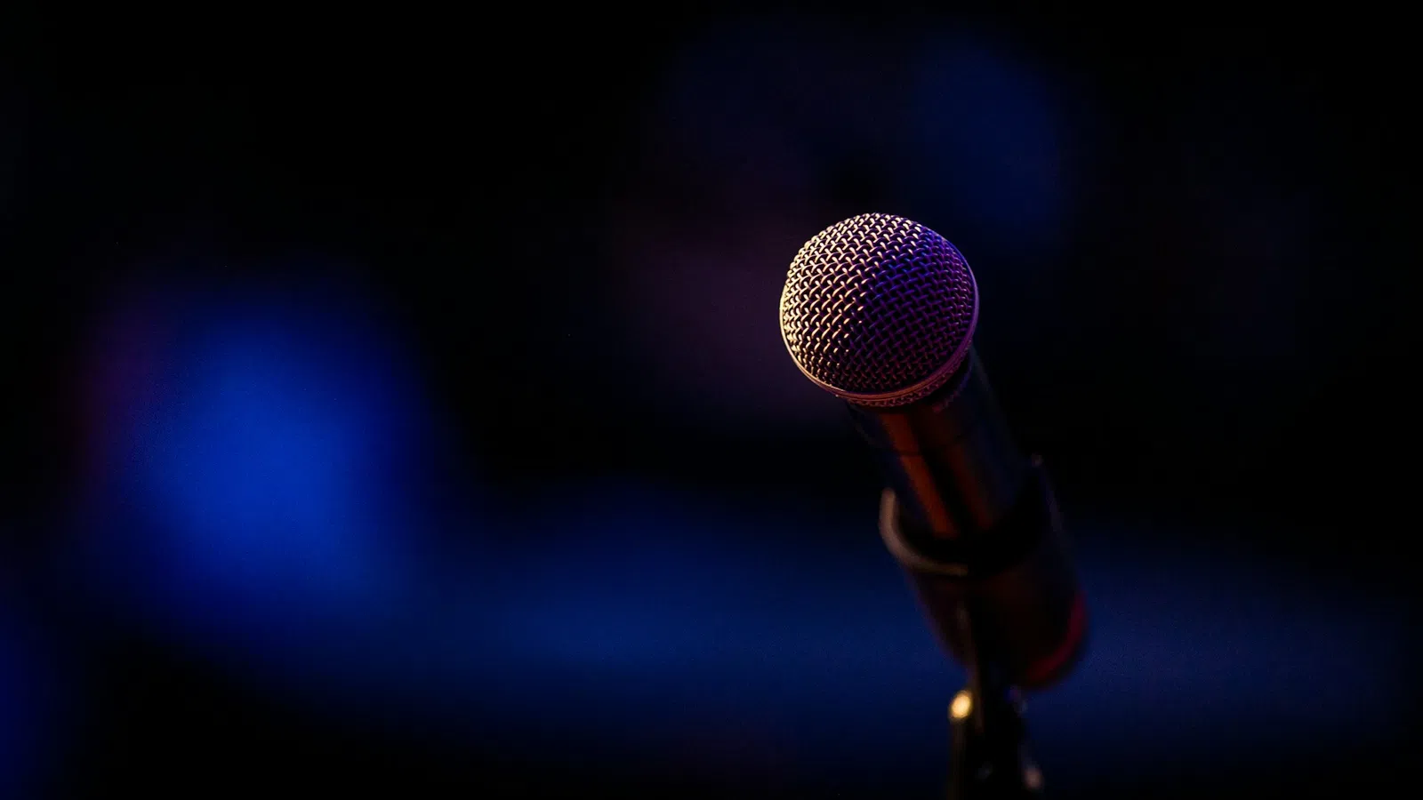 Close-up of a stage microphone with dark blurred background and purple-blue lighting effect.
