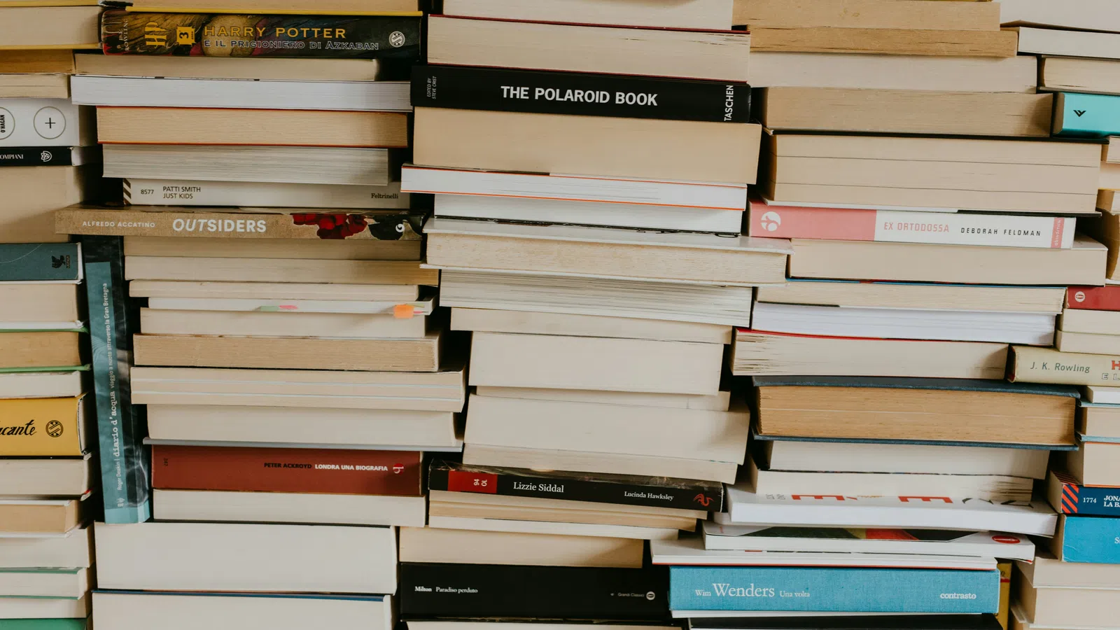 Stacks of assorted books piled horizontally and vertically on a shelf with varied colored covers and spines.