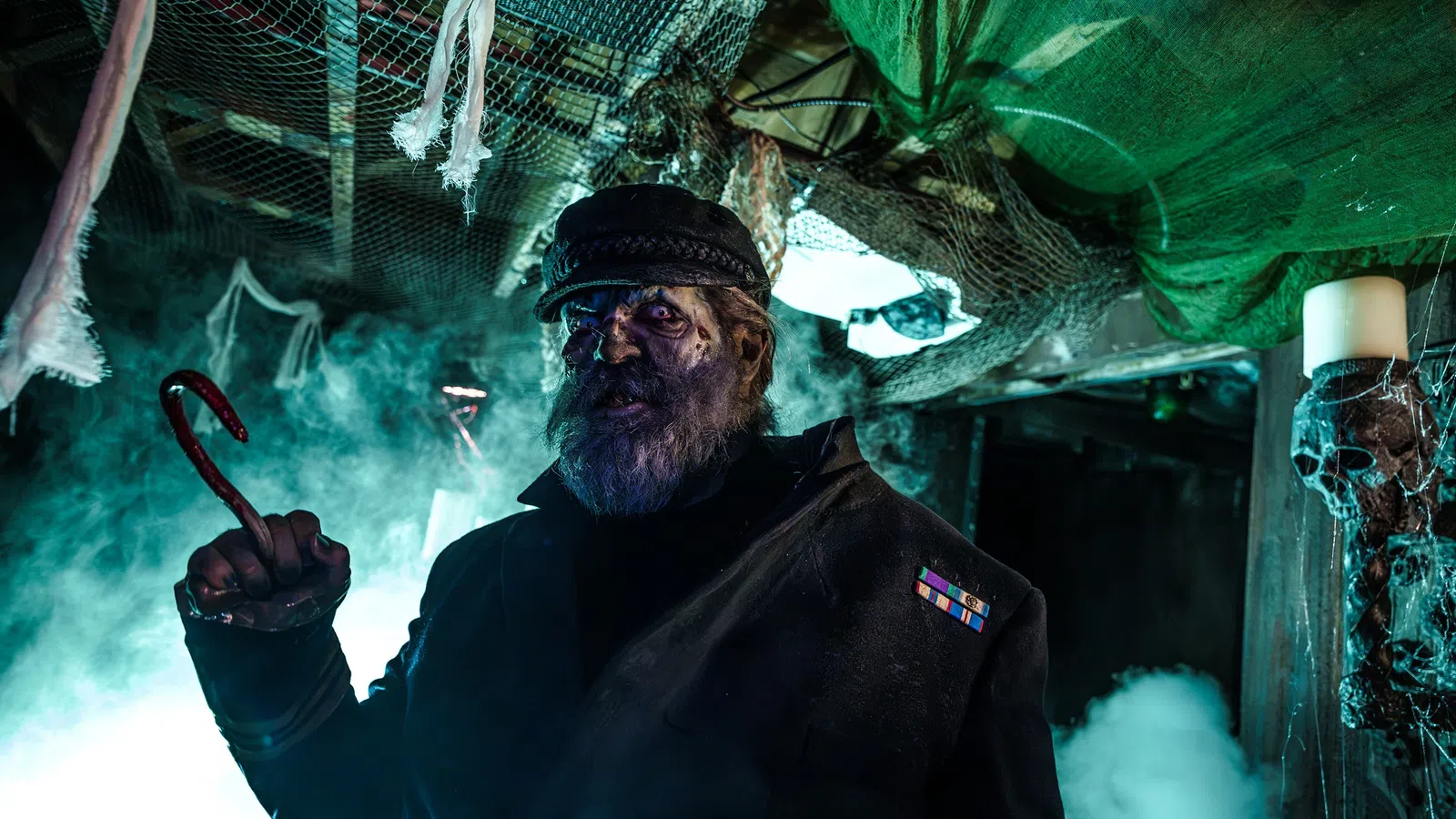 Dark haunted captain with a hook hand and eerie blue lighting in a spooky, fog-filled ship interior.