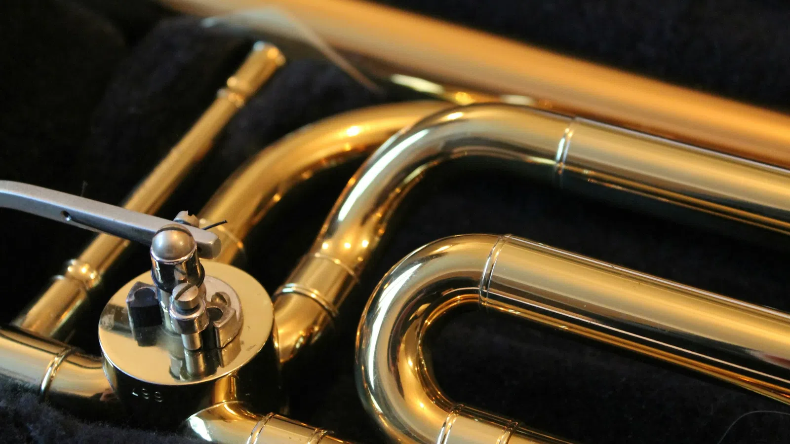 Close-up of shiny brass trumpet valves and tubing on a black fabric background with reflective golden finish
