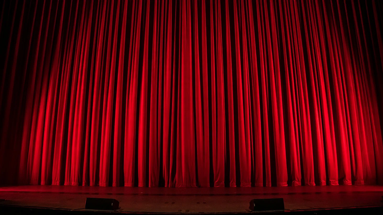 Closed red theater curtains illuminated on a stage ready for a performance.