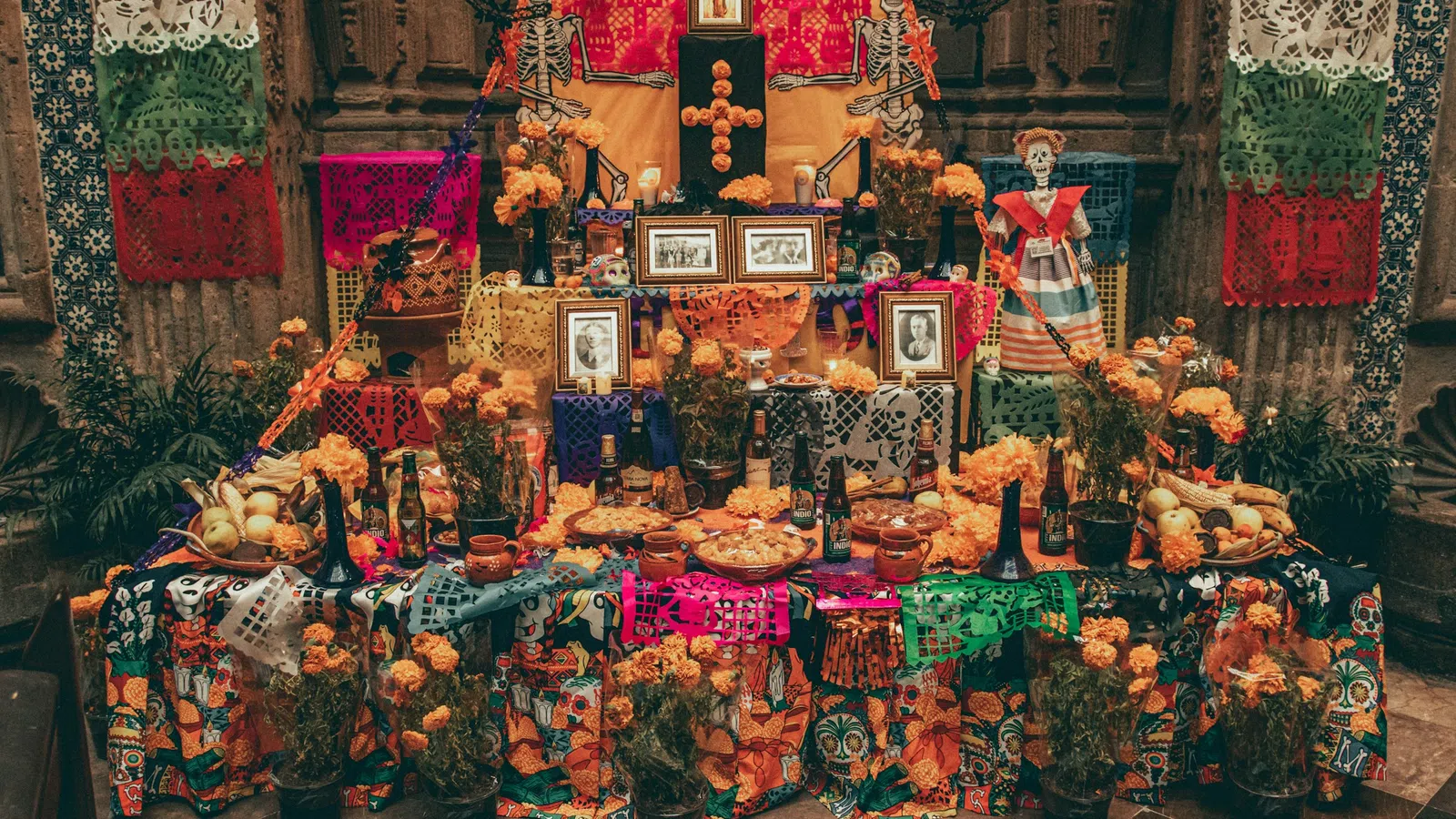 Traditional Mexican Day of the Dead altar decorated with marigolds, papel picado, photos, skeletons, and food offerings.