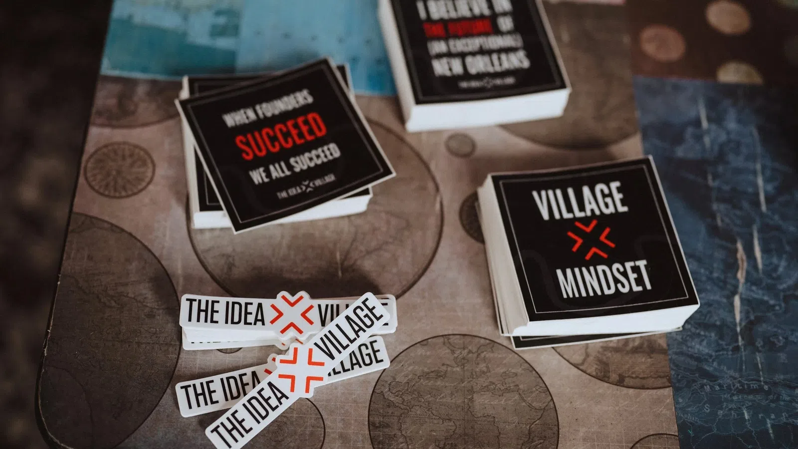 Stacks of motivational and branding stickers on a table featuring phrases like Village Mindset and The Idea Village.
