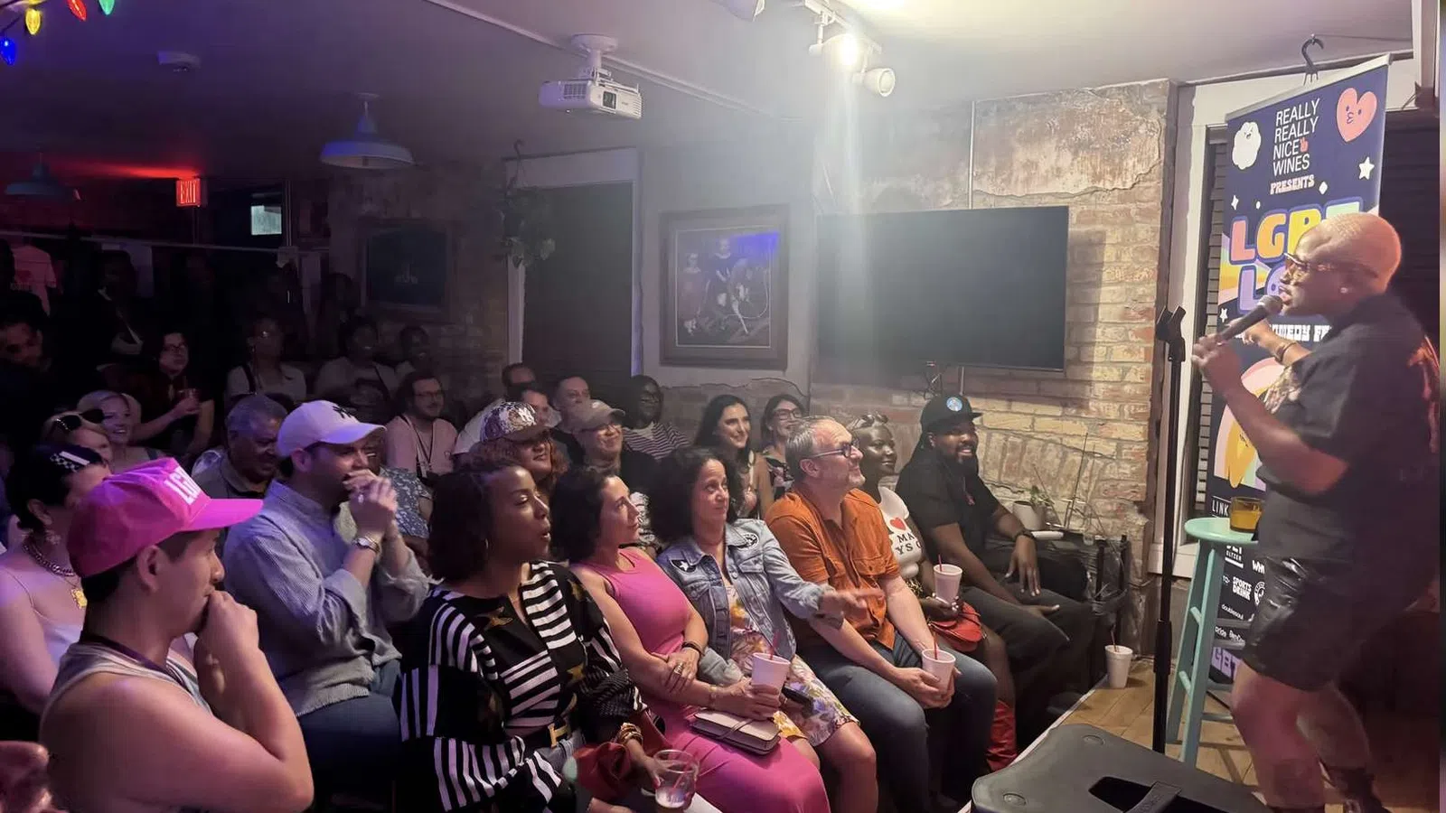 Crowd enjoying a live comedy show in a small venue with colorful lights and a performer on stage.
