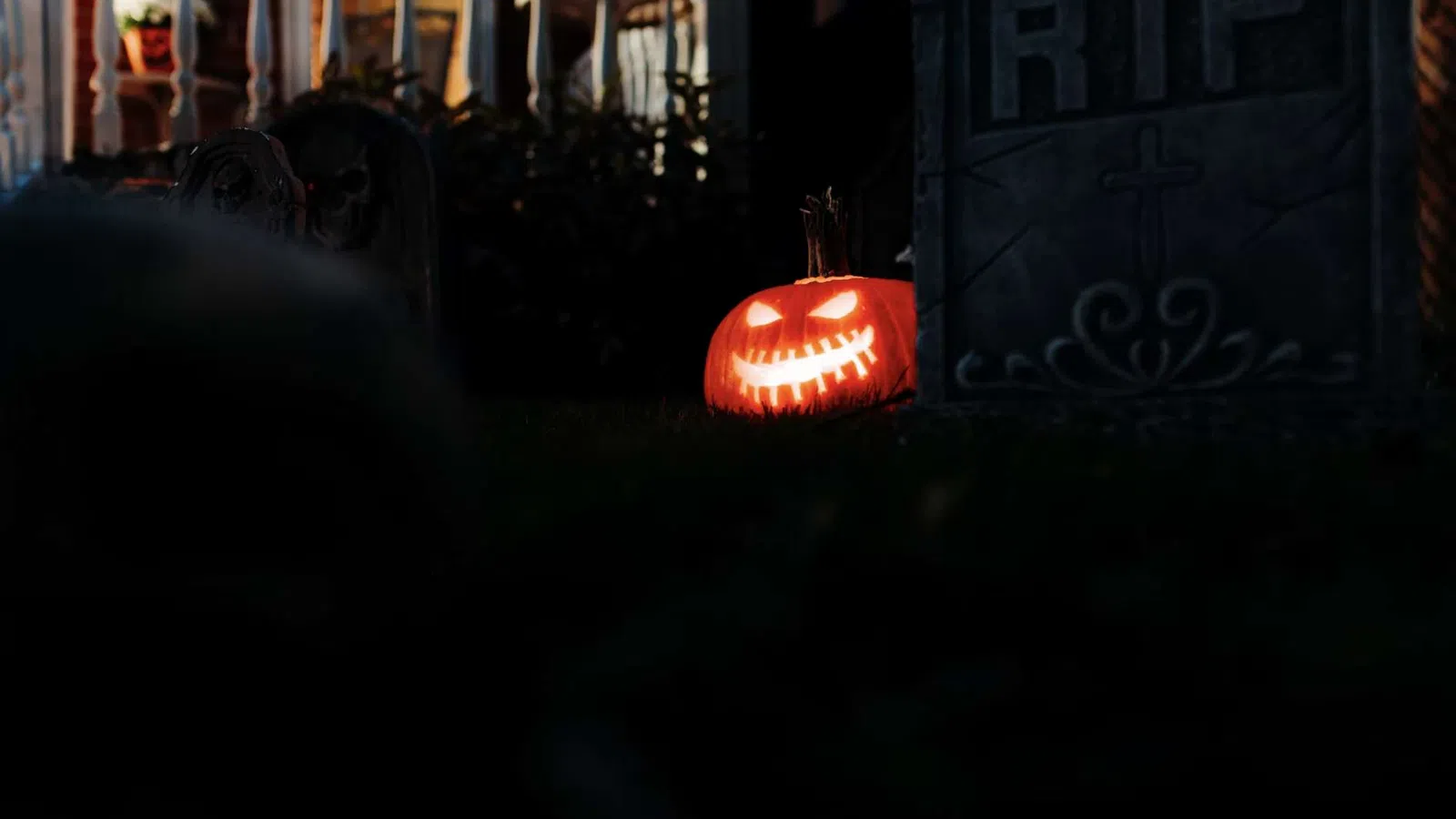 Glowing carved jack-o'-lantern beside a tombstone with RIP in a dark Halloween yard scene.