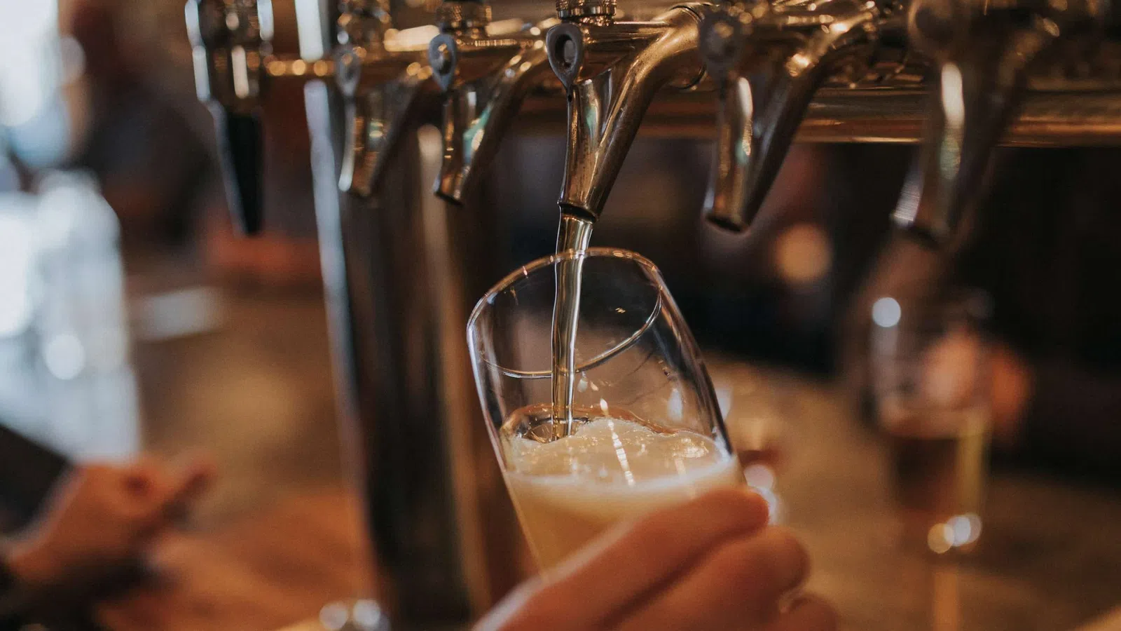 Beer being poured from a tap into a tilted glass at a bar with blurred background.