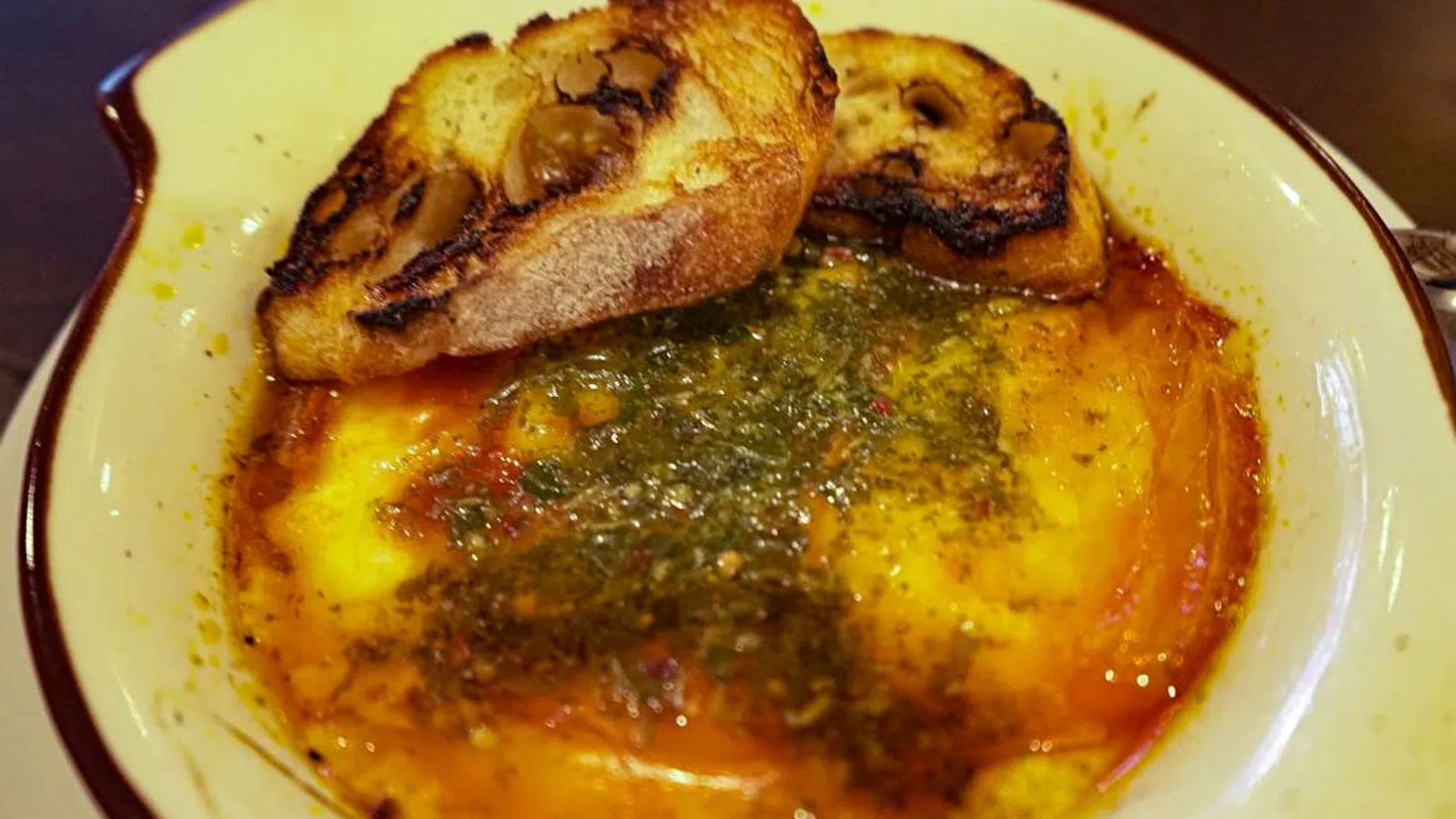Baked melted cheese with herbs and oil served with crispy toasted bread slices in a rustic dish.