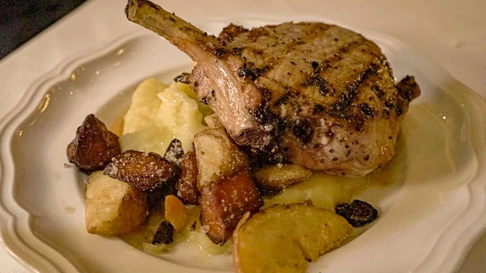 Grilled pork chop with mashed potatoes and roasted root vegetables on a white plate.
