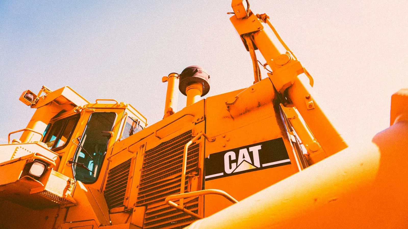 Close-up of a yellow Caterpillar bulldozer with visible CAT logo under bright sunlight.