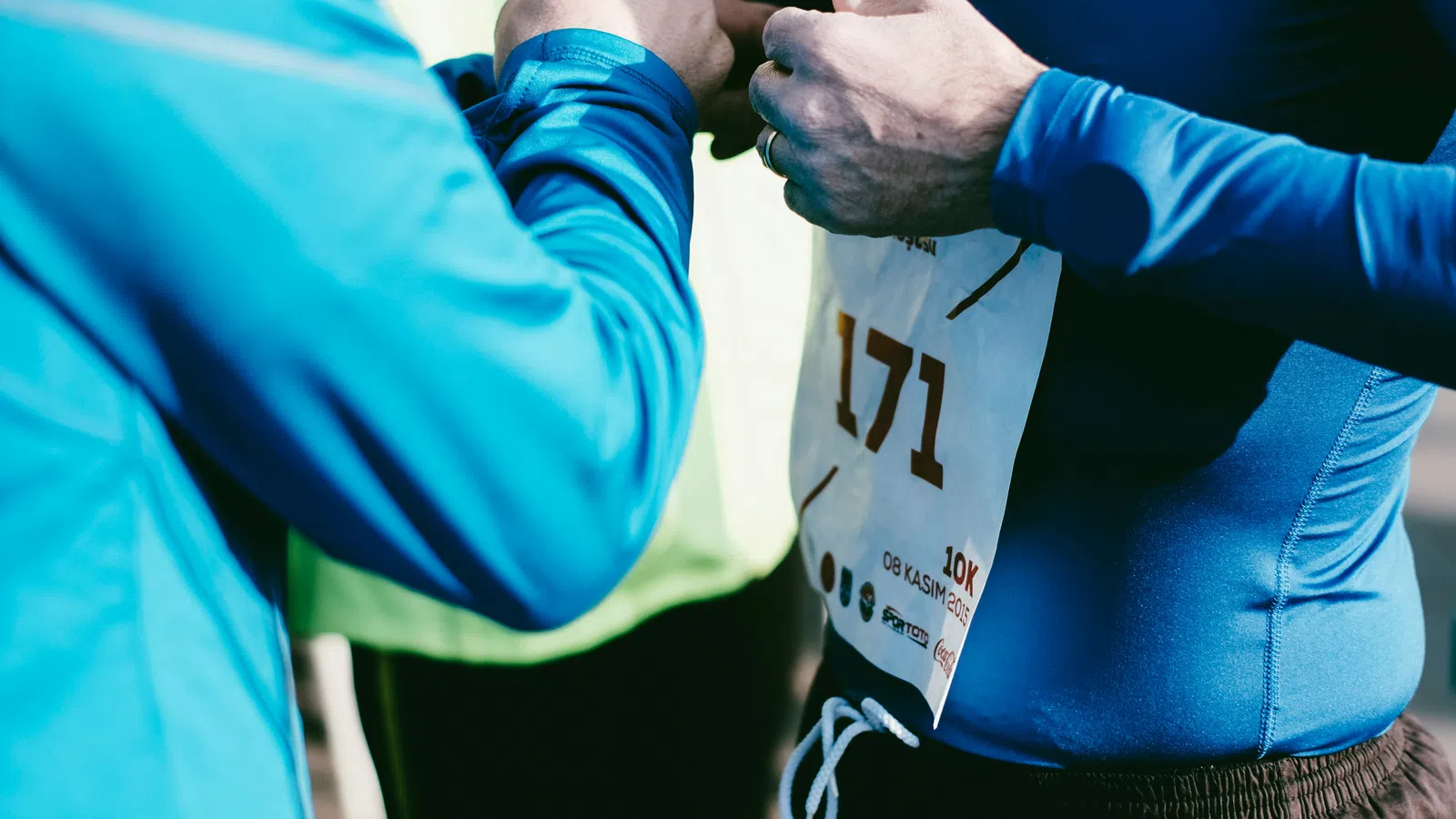 Runners adjusting race bib number 171 before a 10k event on a sunny day with blue athletic gear.