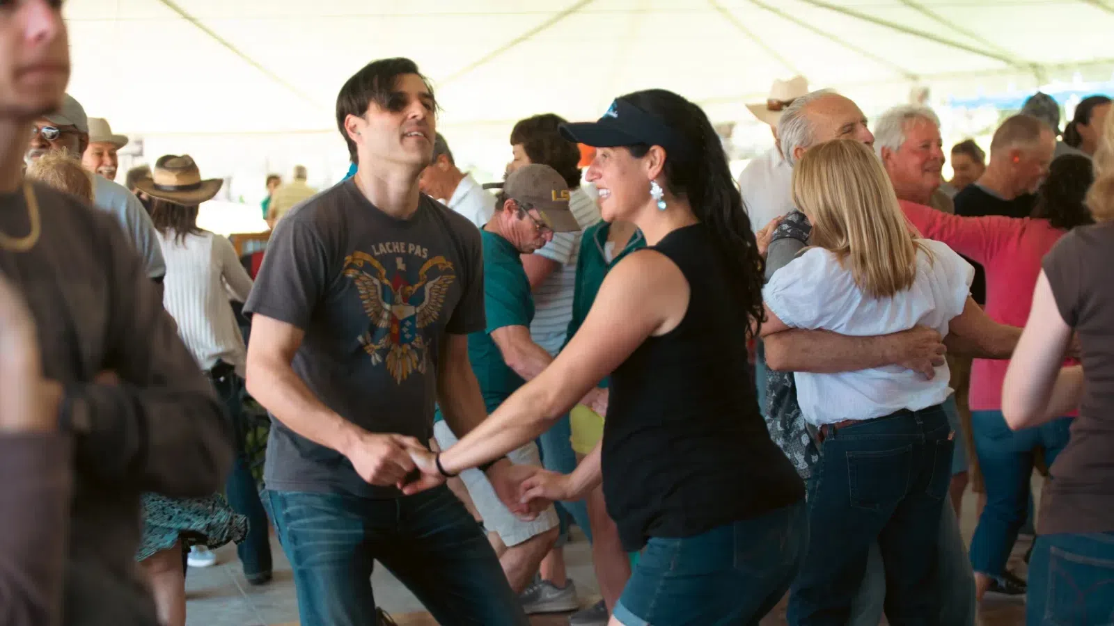 Couples dancing energetically in a lively indoor social dance event under a white tent
