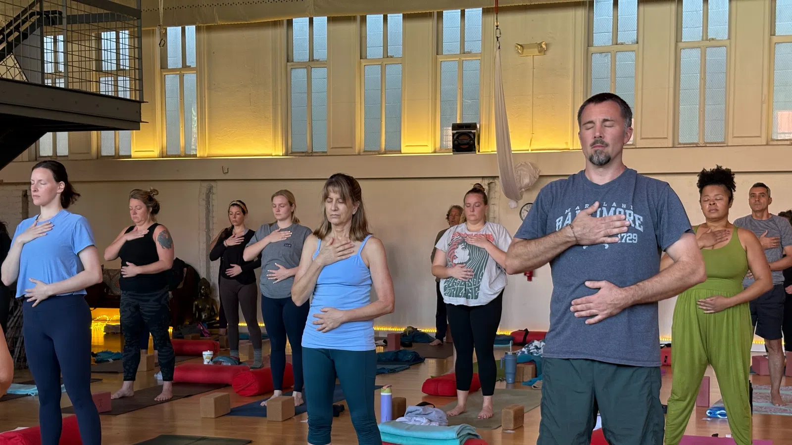 Group of diverse adults practicing mindful breathing with hands on chest and abdomen in a sunlit yoga studio.