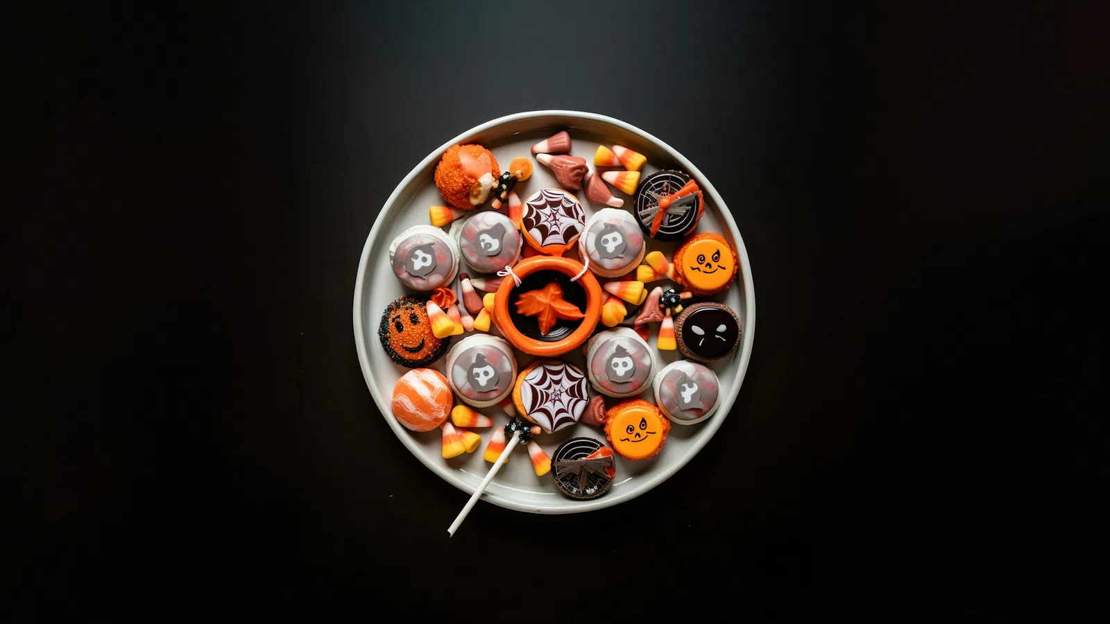 Plate of Halloween-themed cookies and candy corn on black background with orange and black decorations