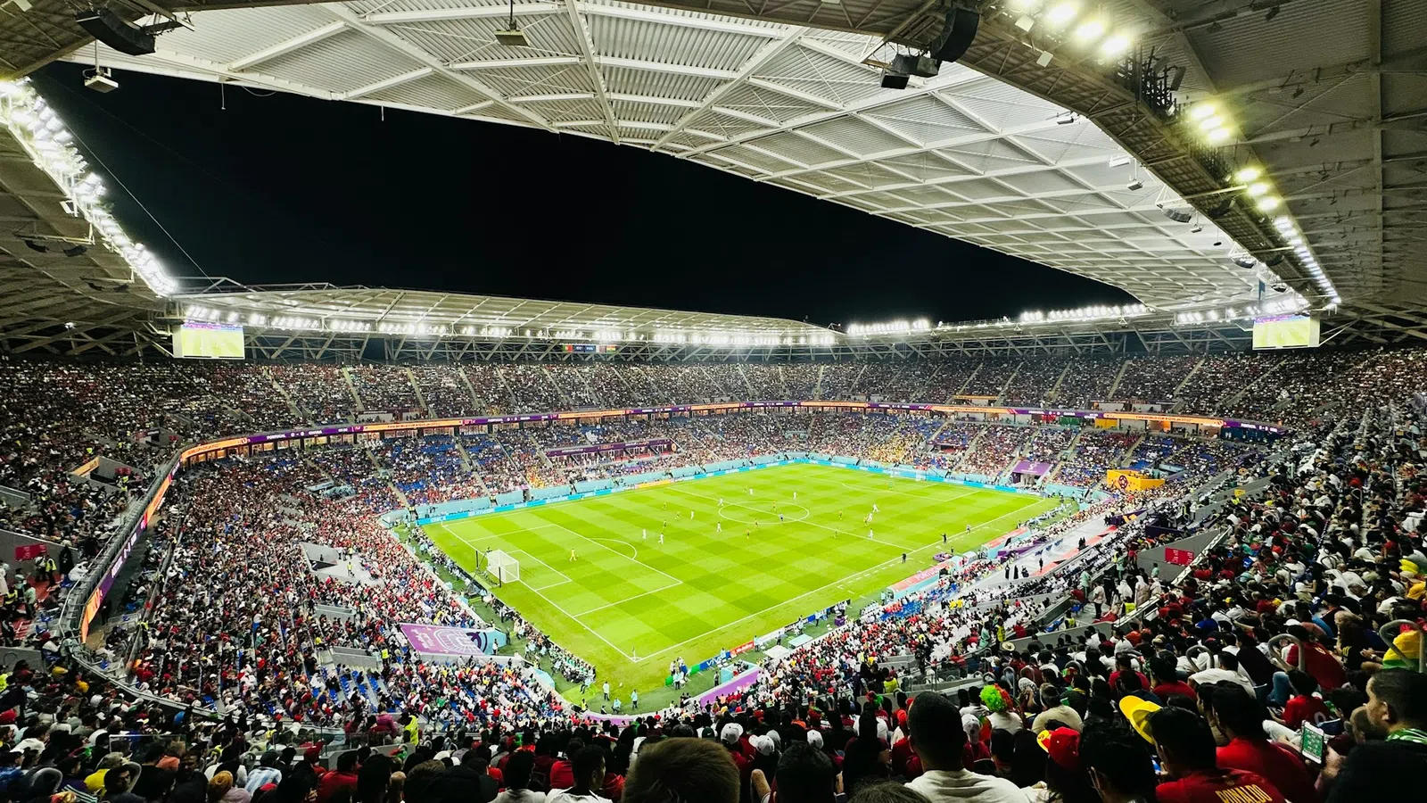 Nighttime soccer match in a packed stadium with bright lights and enthusiastic crowd.