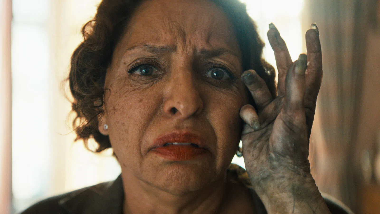 Worried woman with dirt-covered hand touching her face in a close-up emotional moment indoors.