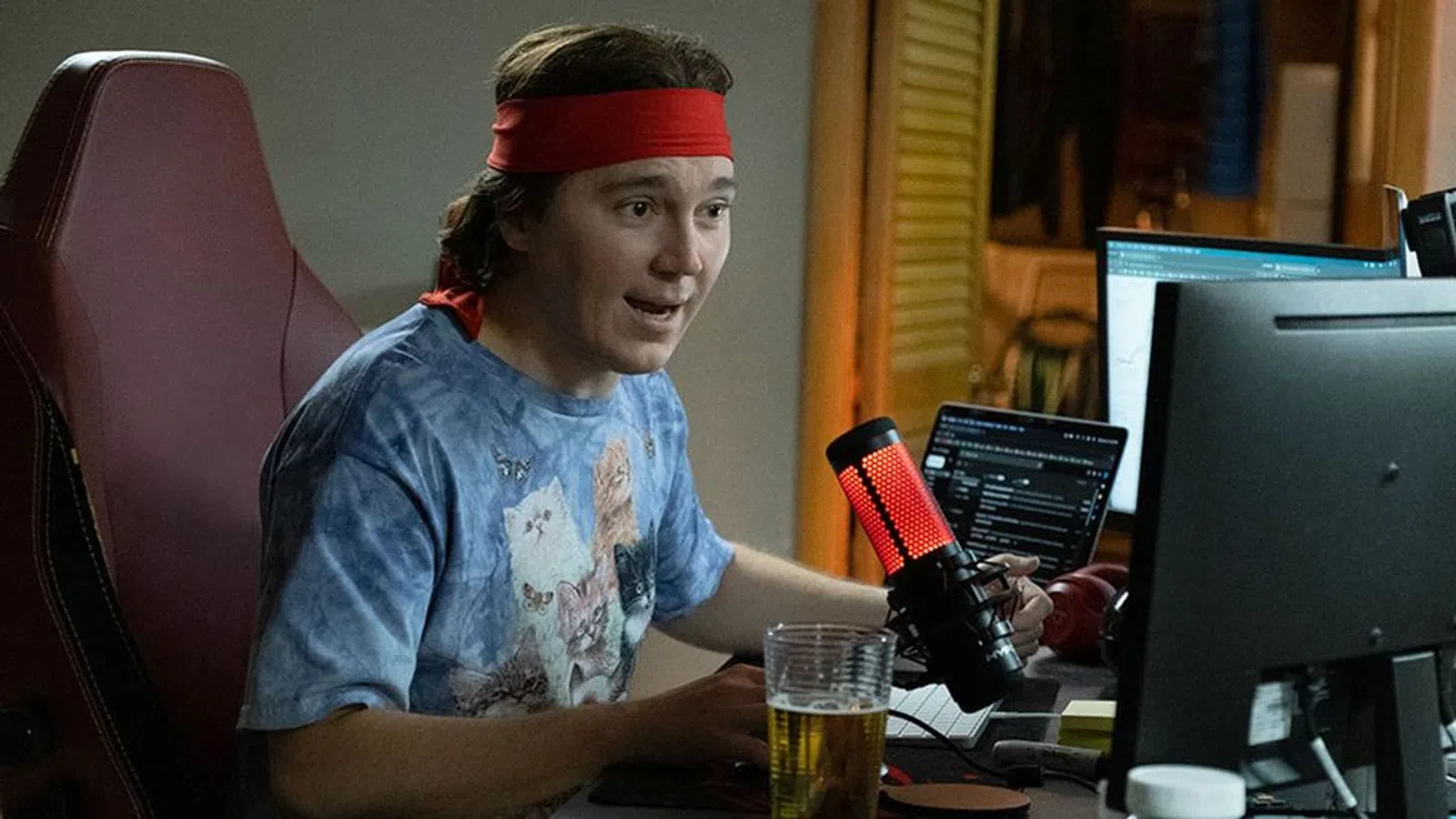 Paul Dano sitting at a desk with a computer and a microphone