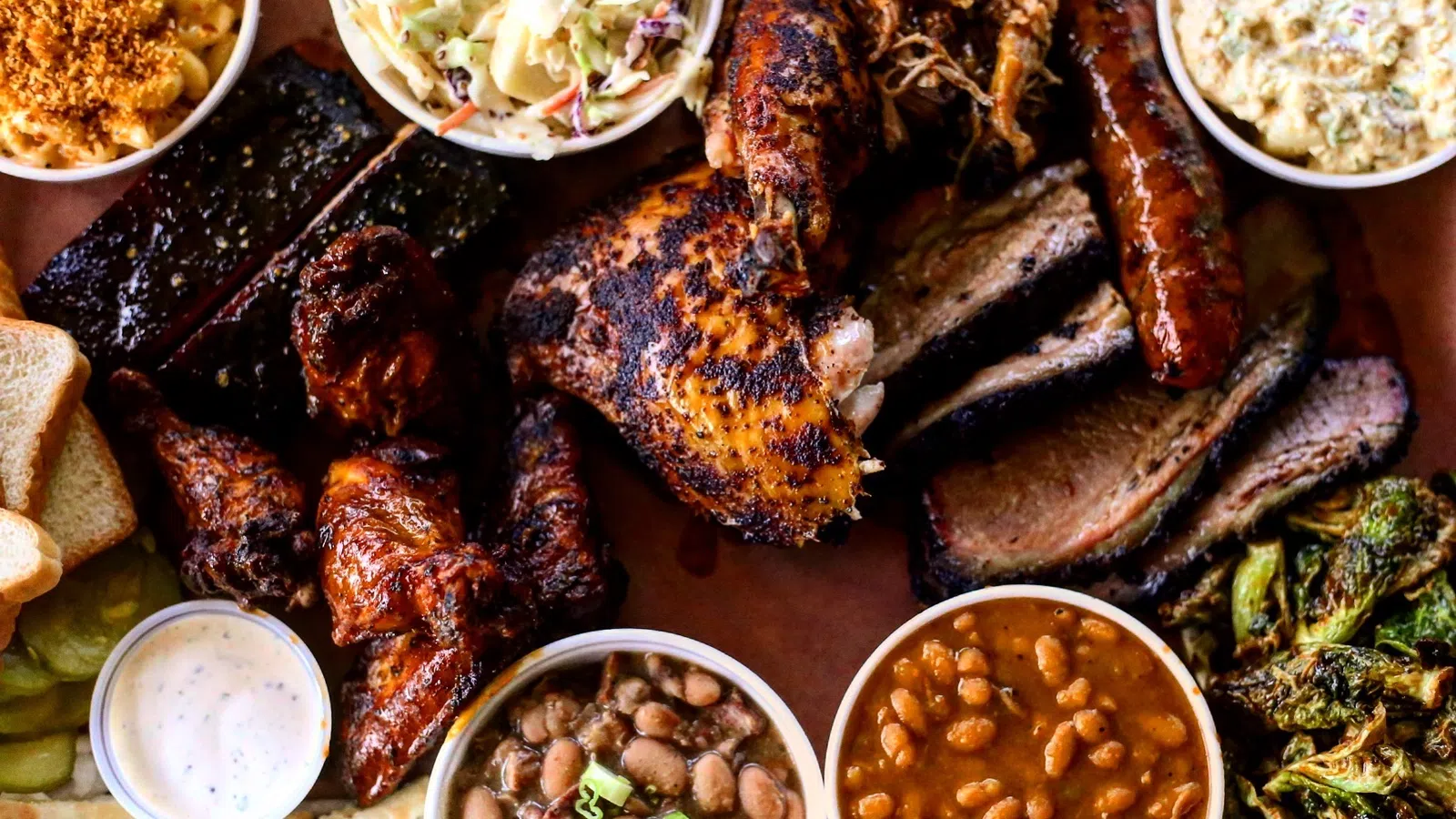 Barbecue feast with smoked chicken, ribs, sausage, brisket, wings, beans, coleslaw, and sides served on a platter.
