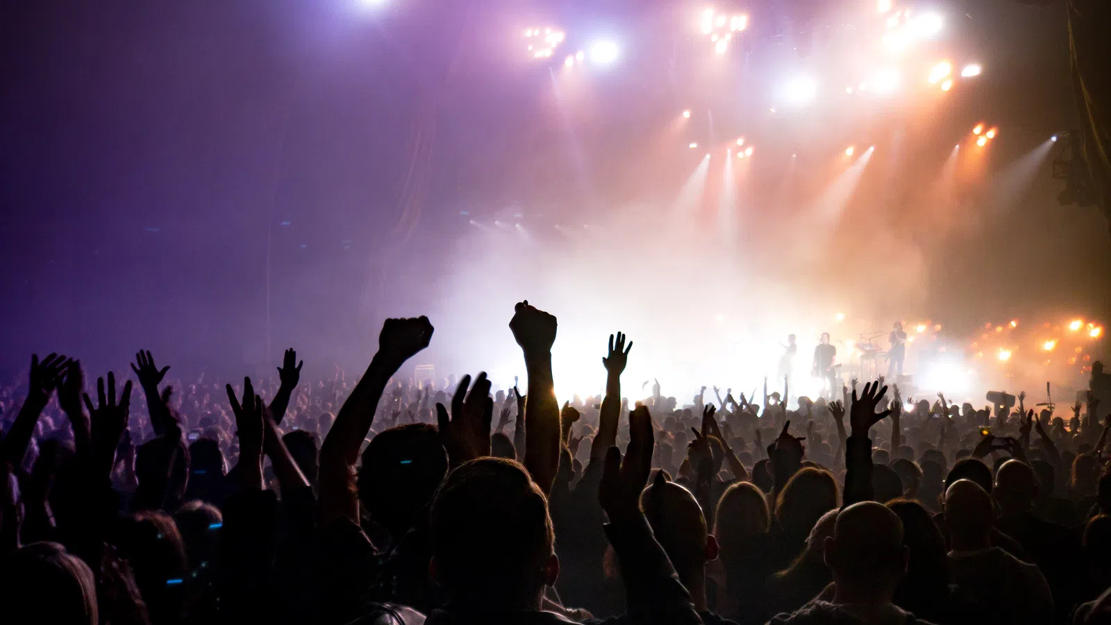 a crowd of people with their hands up in the air in front of a stage with lights