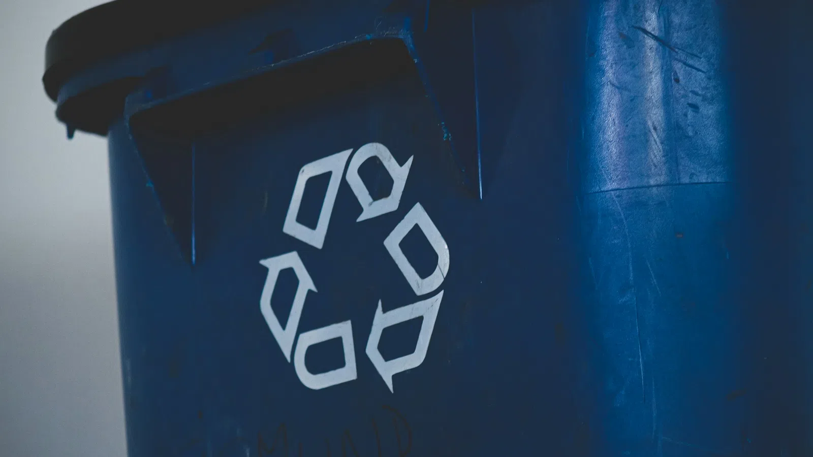 Close-up of a blue recycling bin with a white recycling symbol on it.